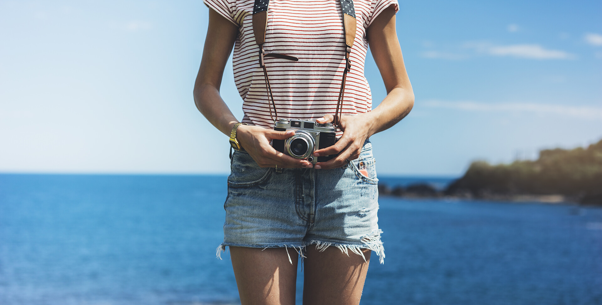 蔚蓝大海前挎着相机站立的女孩住，拿着相机的女孩