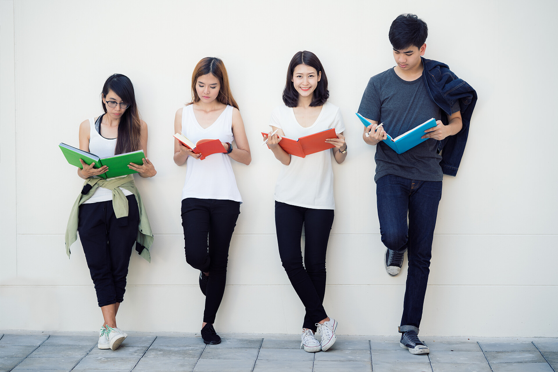 亚洲学生和朋友一起靠墙站着读书在大学读书的亚洲学生