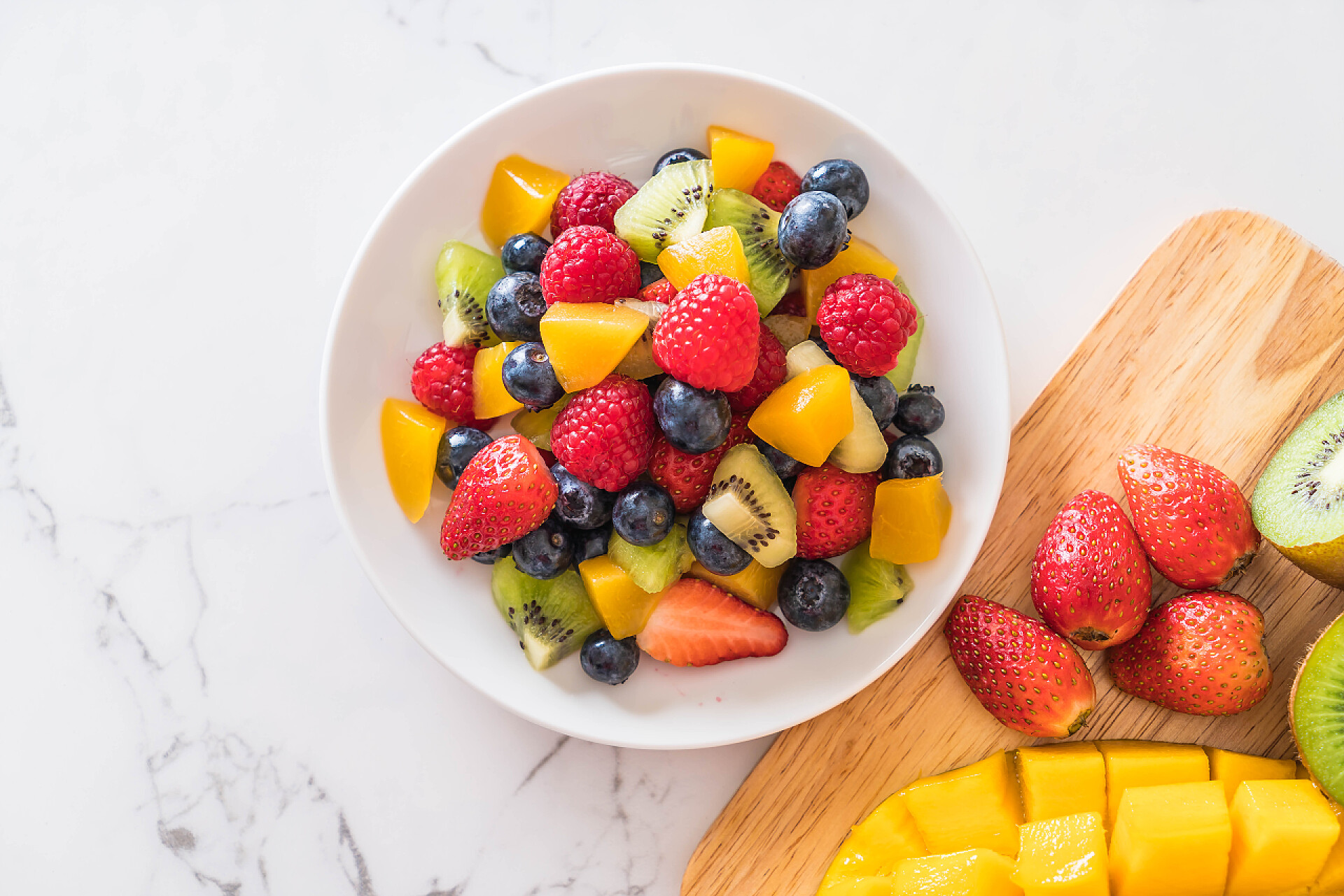 白色岩板桌上的一碗水果沙拉混合新鲜水果 （草莓、 覆盆子、 蓝莓、 猕猴桃、 莽