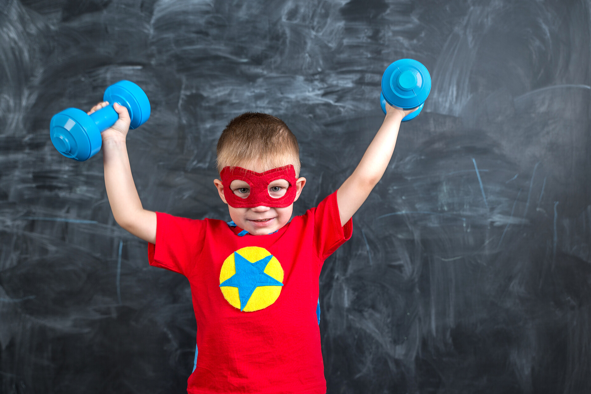 穿着超人衣服举着蓝色哑铃的男孩男孩超级英雄与哑铃