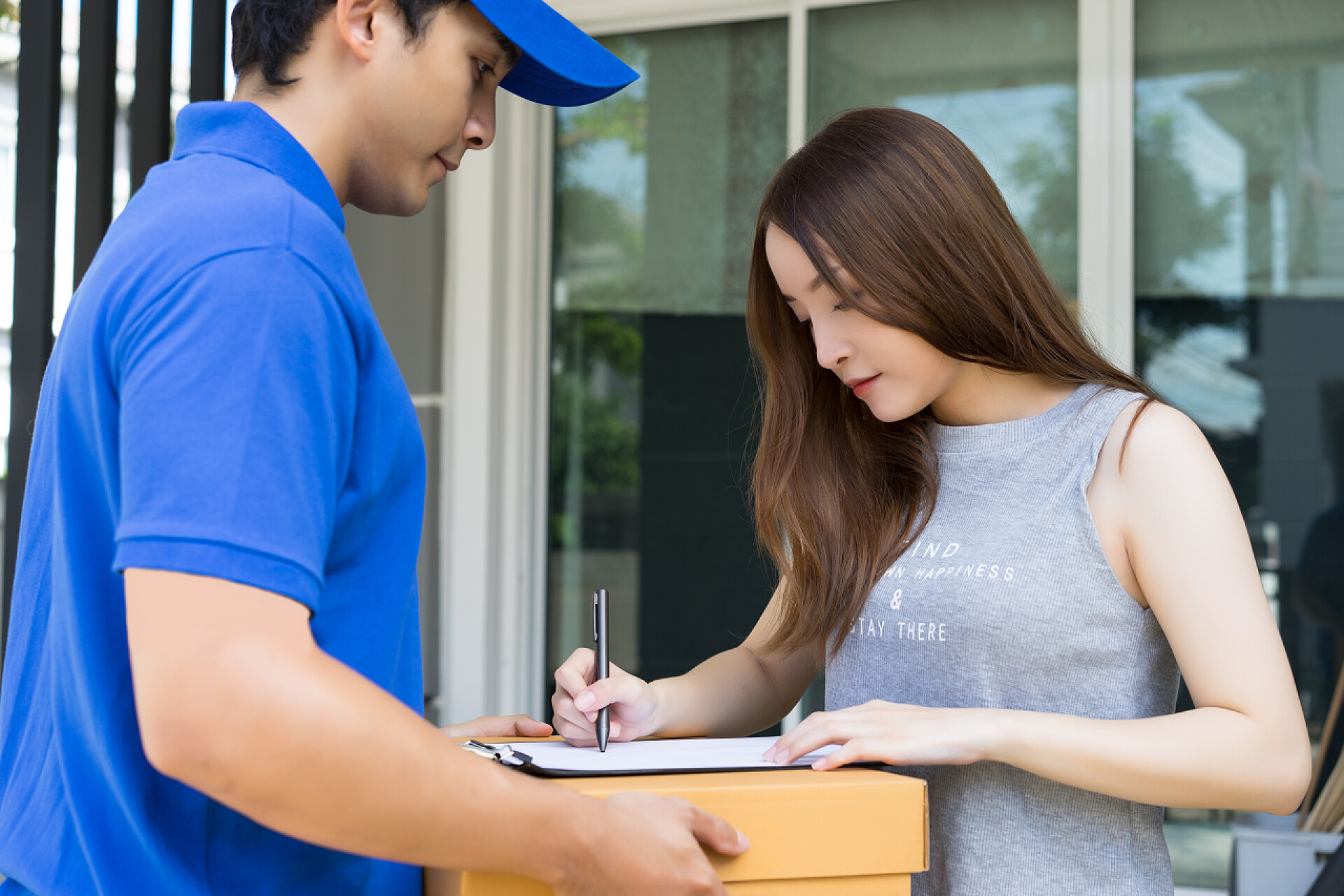 蓝色制服快递员和在纸板箱上签字的客户友好的年轻送货人在蓝色制服拿着纸板