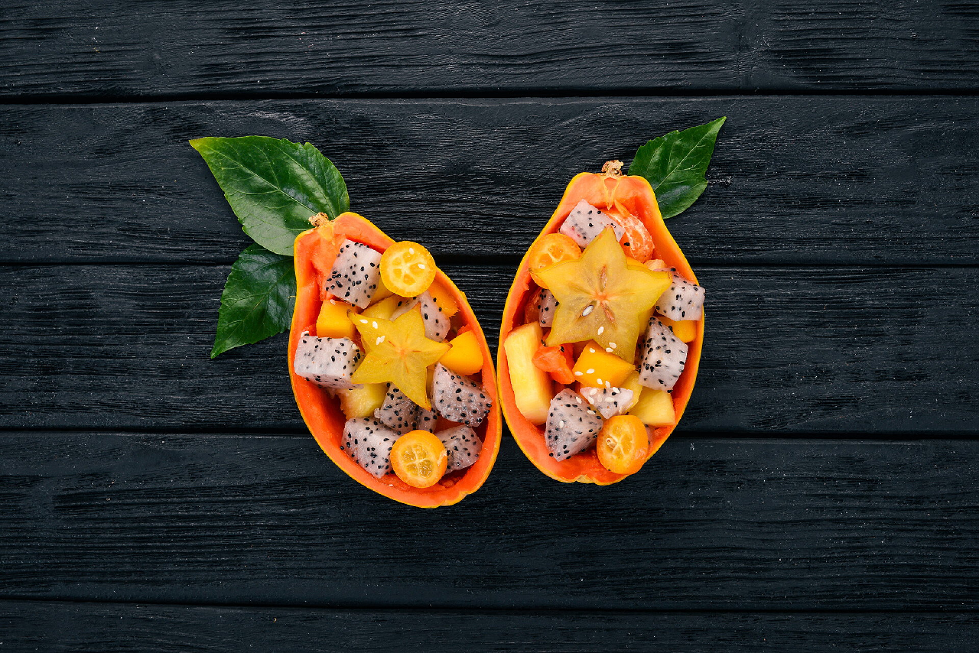 在木瓜碗里的水果沙拉半木瓜的热带水果沙拉。龙果, 毛丹, 罗望子, 仙人掌果, 鳄梨, 芒果。在木制背景上。顶部视图.