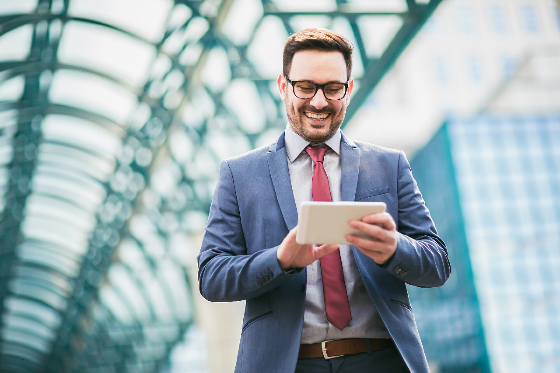一个低头看手机平板笑的男商人商业人站在商业大厦。从事数码平板电脑业务的人.