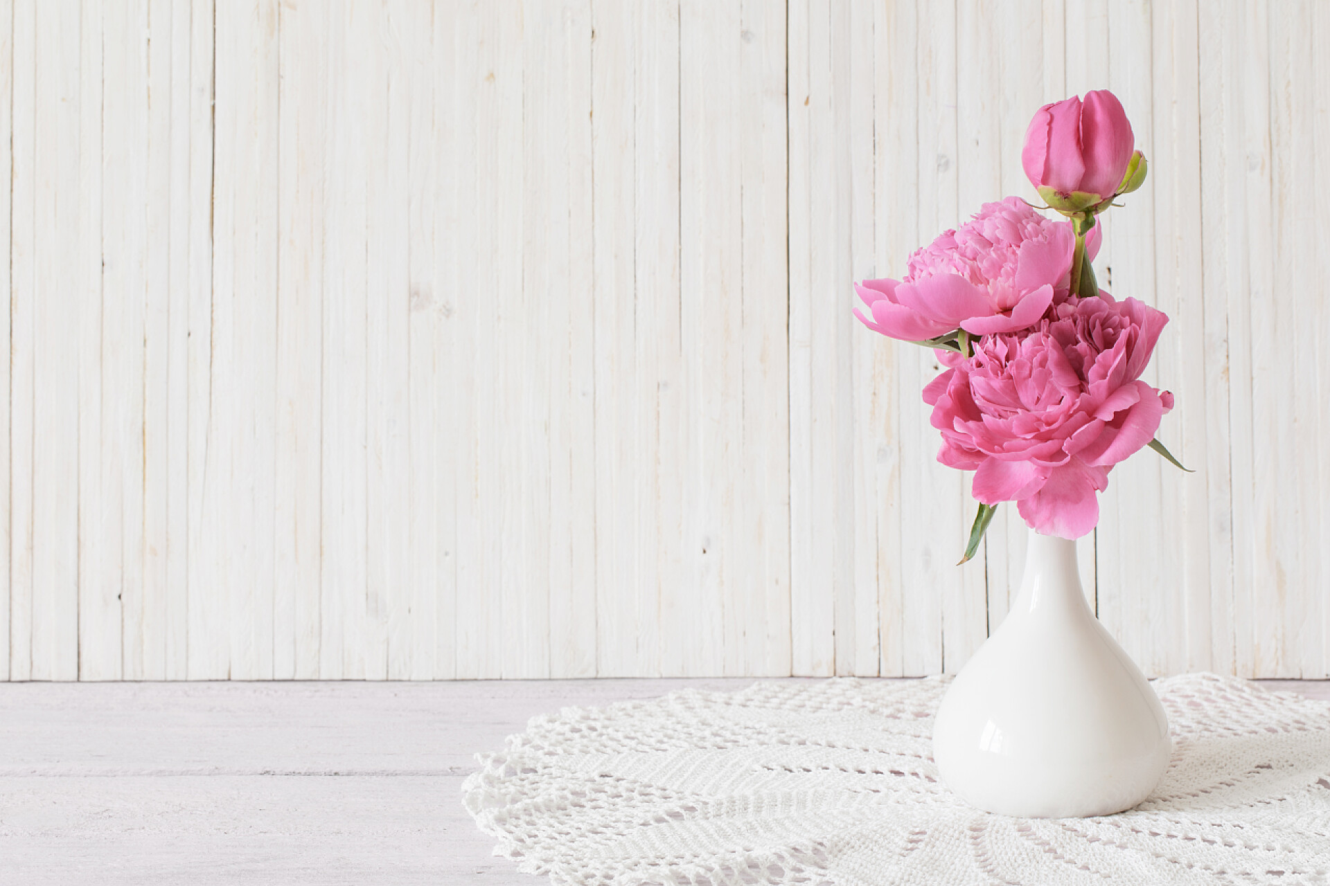 木制墙壁前的白色花瓶中的粉红色牡丹木制白色花瓶中的粉红色牡丹