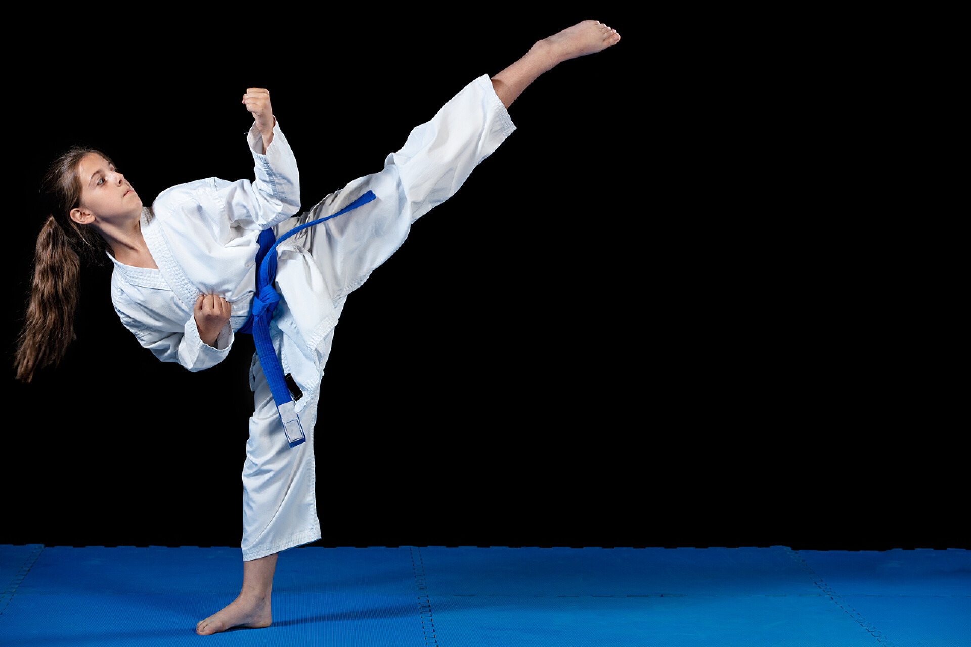 黑色背景前练跆拳道的小女孩穿白色和服的年轻女孩空手道