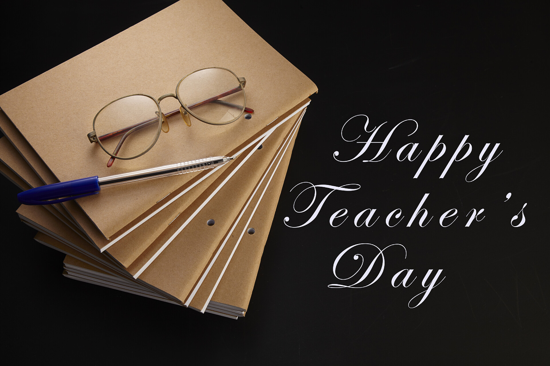 黑色背景上的笔记本钢笔和眼镜特写带笔记本、钢笔和眼镜的教师日间贺卡, 带复制空间的黑色背景