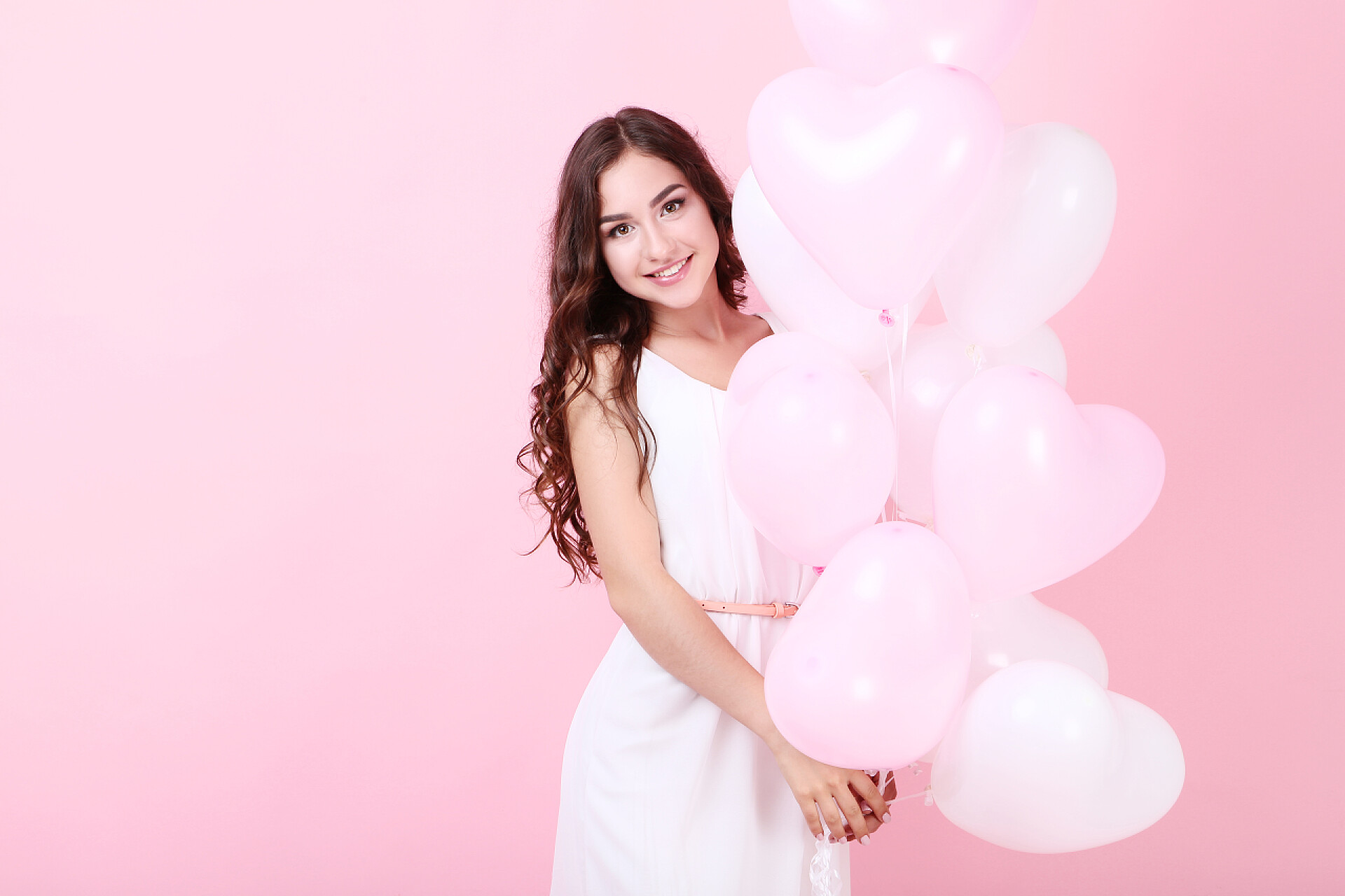 在粉红色背景上手拿气球的女孩年轻女孩举行心脏气球在粉红色背景