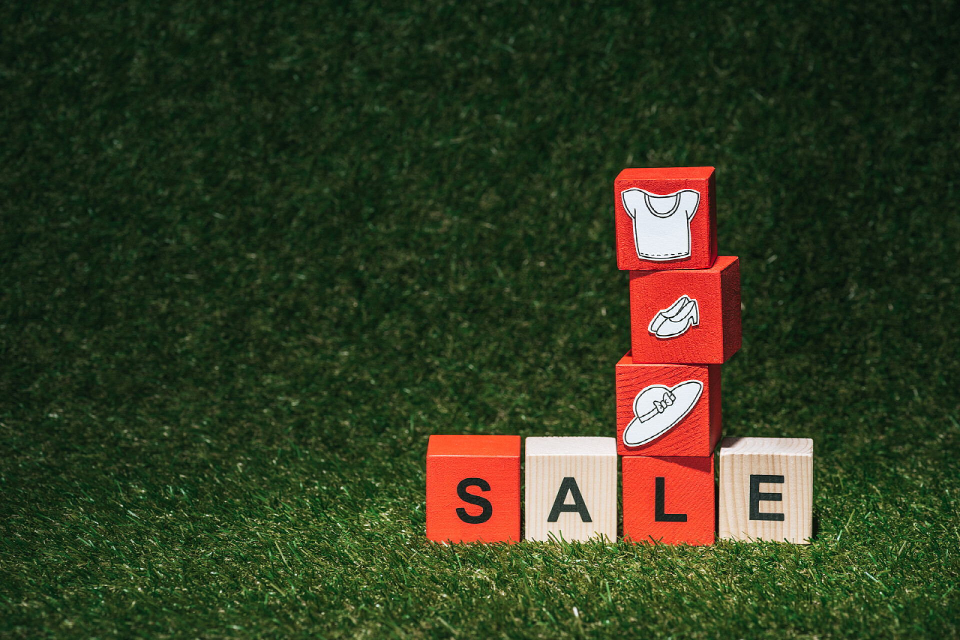 在绿色草上的积木块红色和木制字母立方体与销售标志和衣裳在绿色草 