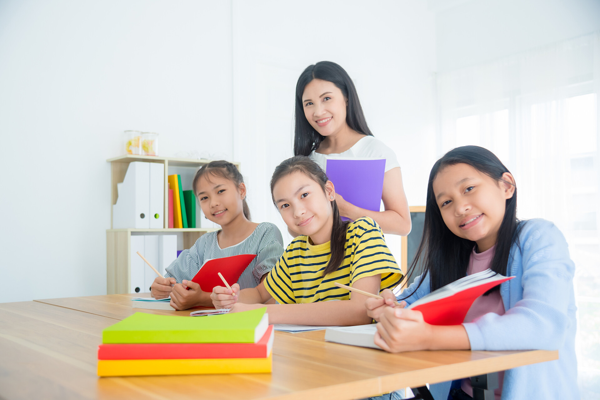 三个亚洲学生和老师坐在教室里看书三个亚洲学生在教室里坐着看书 