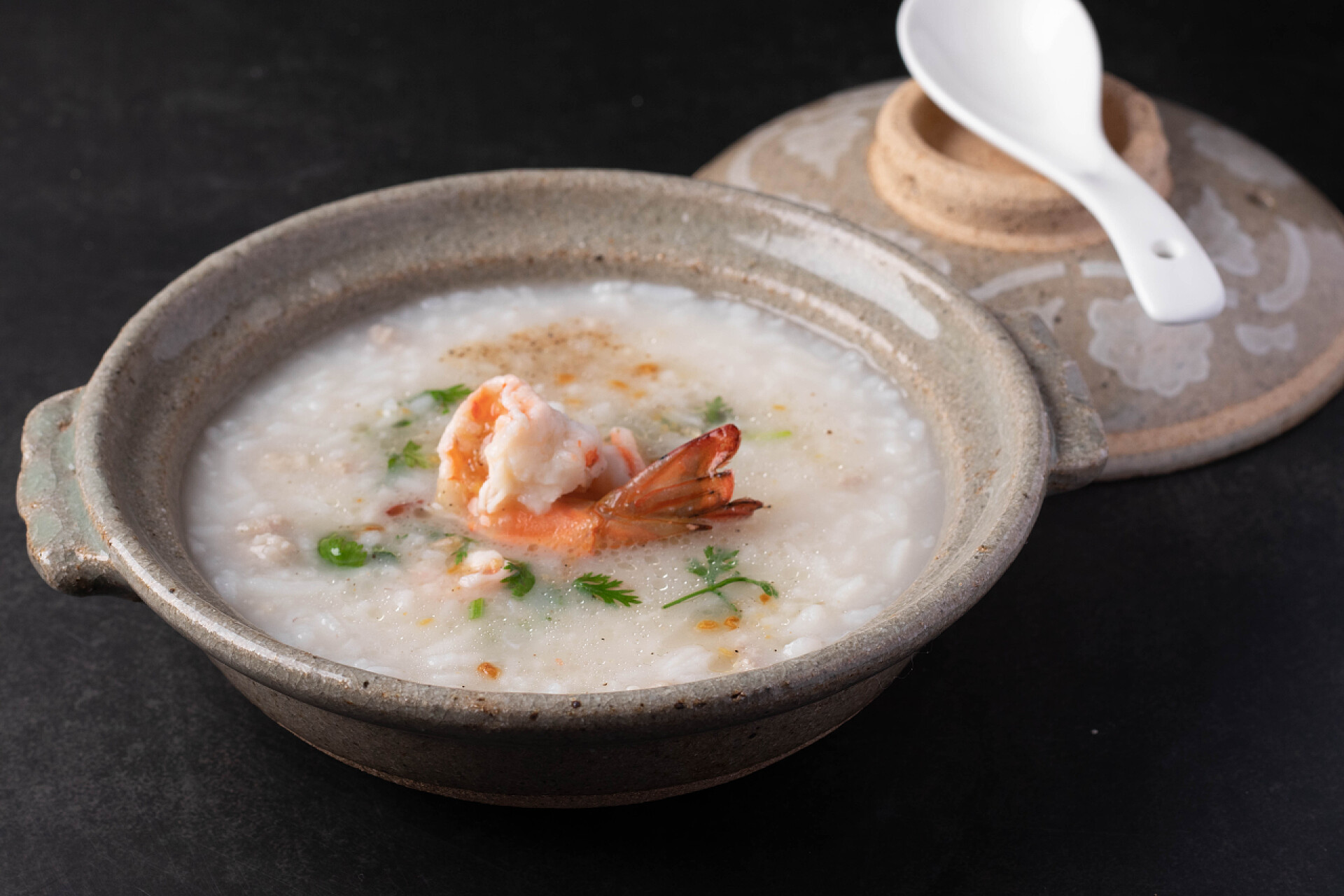 砂锅里的鲜虾粥虾仁炒饭或海鲜炒饭，背景为黑色.