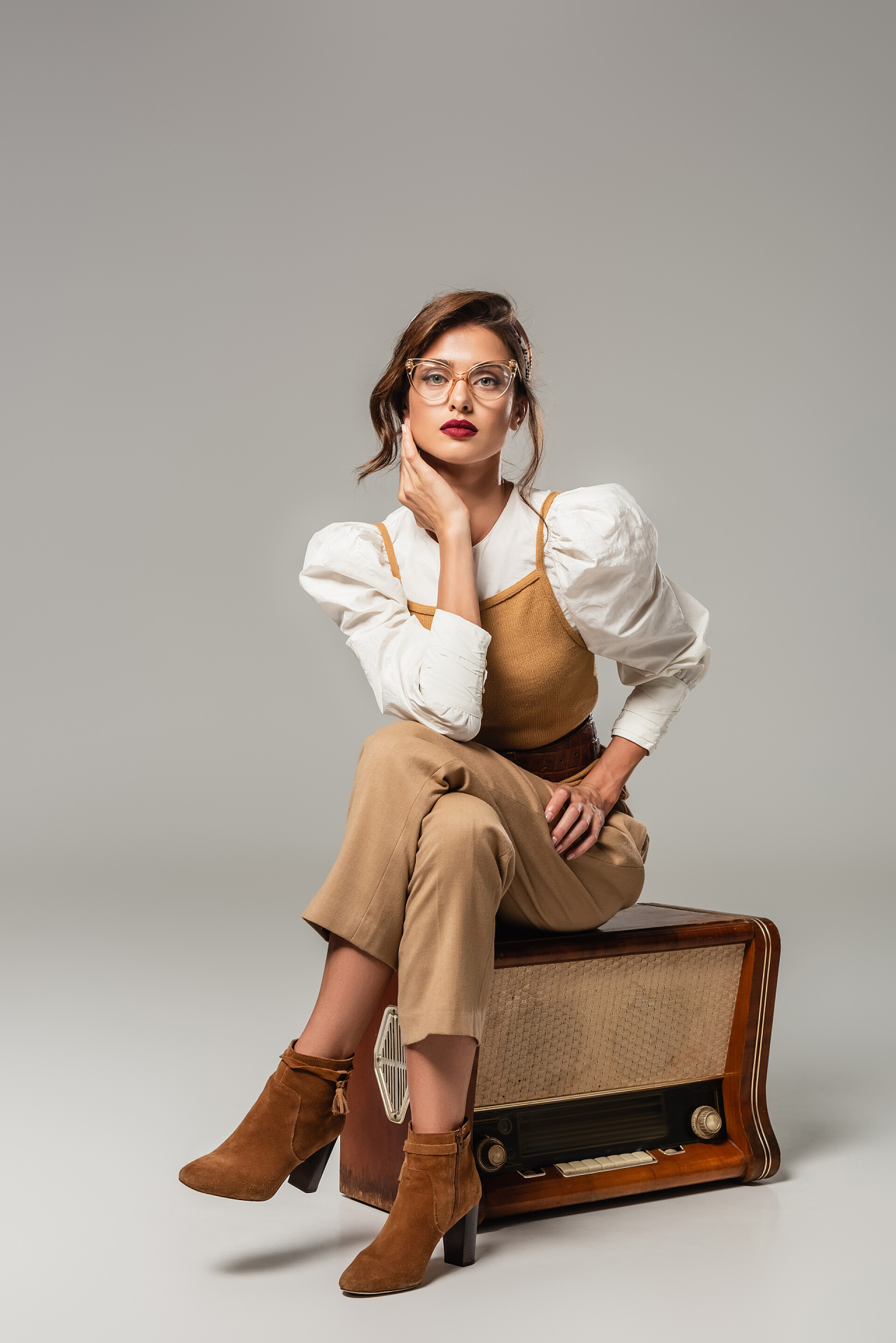 坐在沙发上的时尚女性时尚女人坐在灰色的老式收音机上看着相机