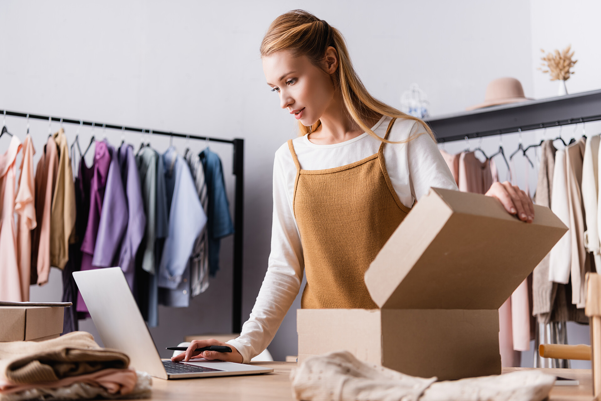 在用笔记本工作的服装店店主陈列室店主在纸板箱附近的笔记本电脑上工作，前景暗淡