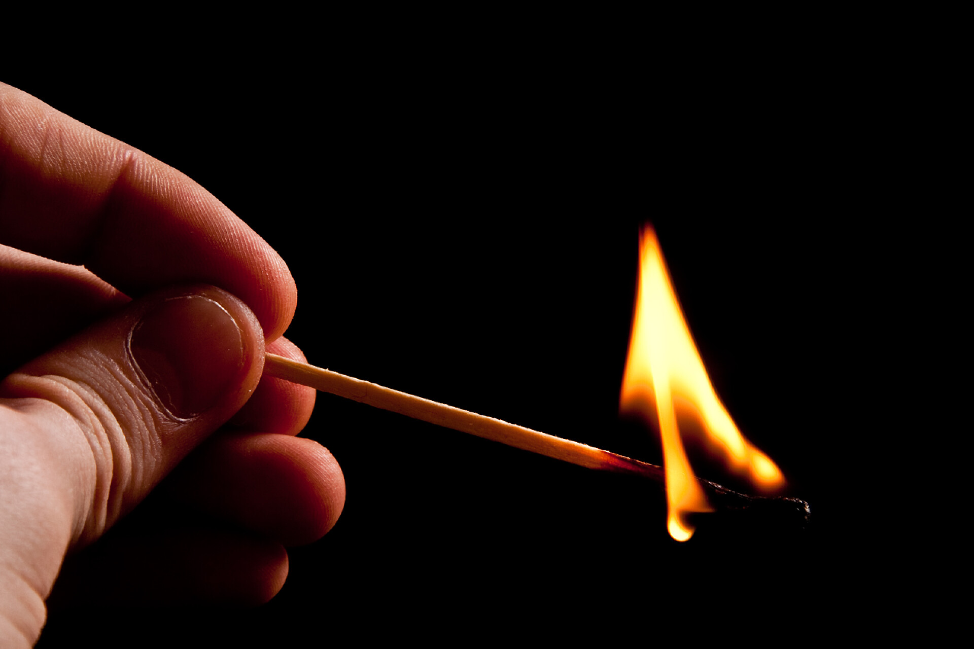 黑色背景上手拿燃烧的火柴火与烟的匹配