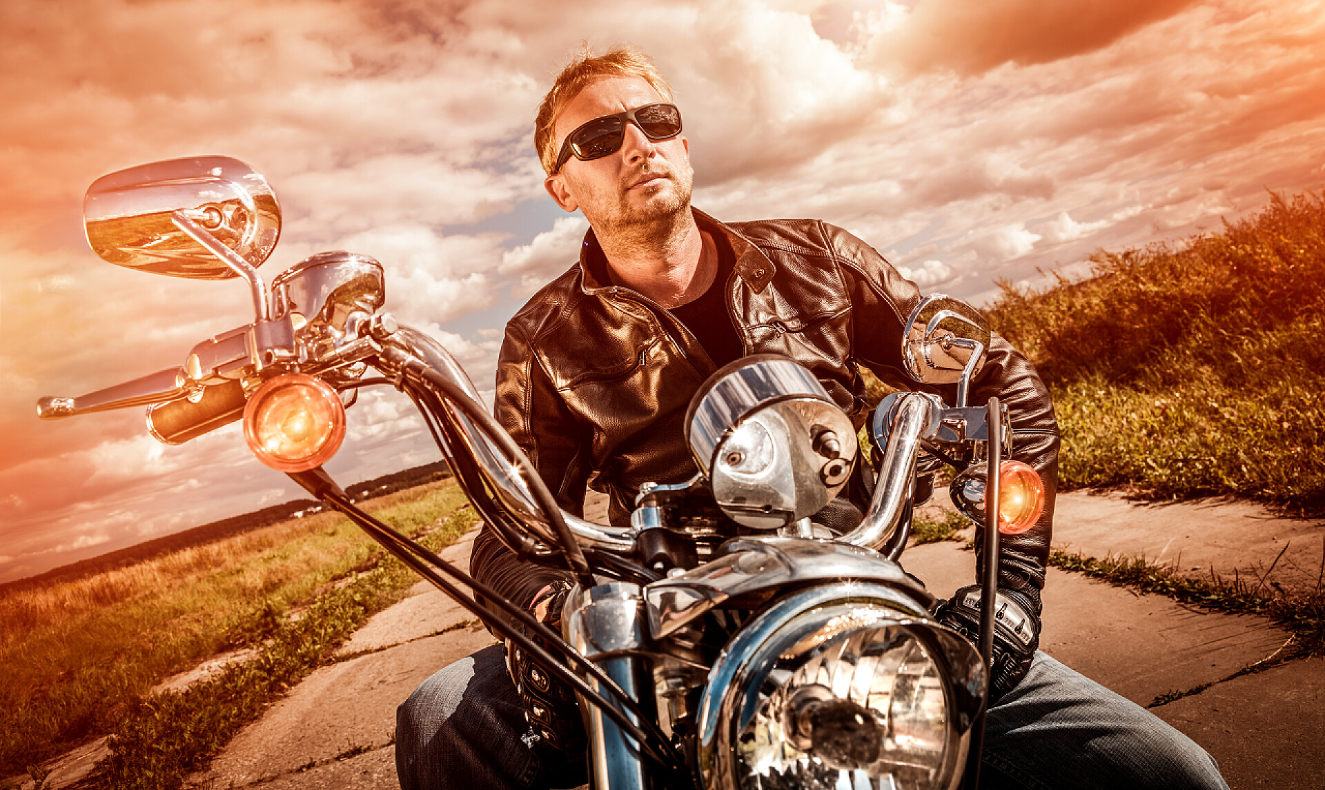 男子穿一件皮夹克坐在他的摩托车上看日落骑摩托车的人