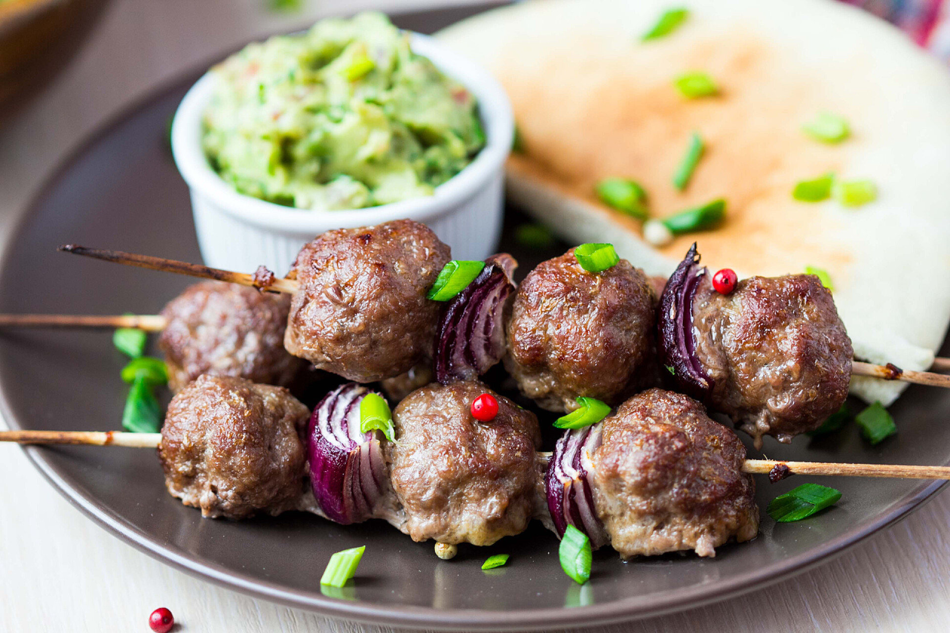 盘子里的牛肉丸和鳄梨酱调味酱肉串、 串用洋葱、 牛肉球酱鳄梨调味酱