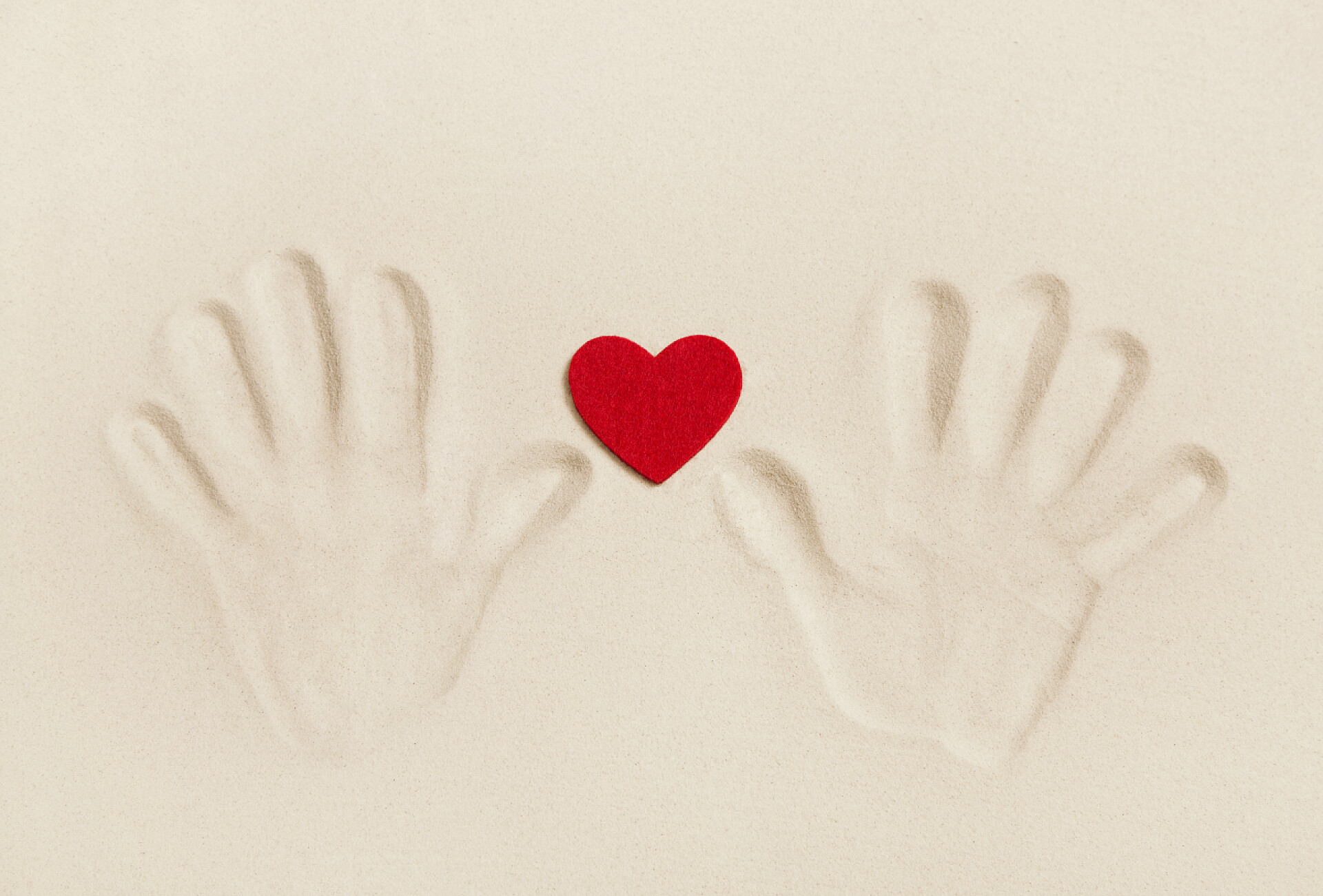 在沙滩上的一颗红色的心和两只手印两只手打印在沙滩上用一颗红色的心。符号的概念