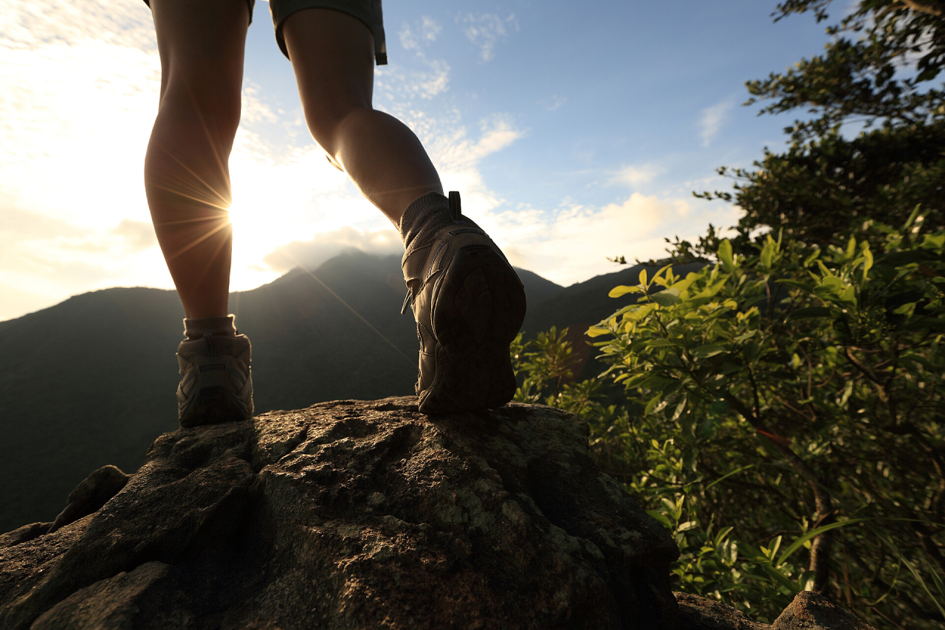 夕阳下徒步旅行的脚步特写女人的徒步旅行者双腿爬上高山