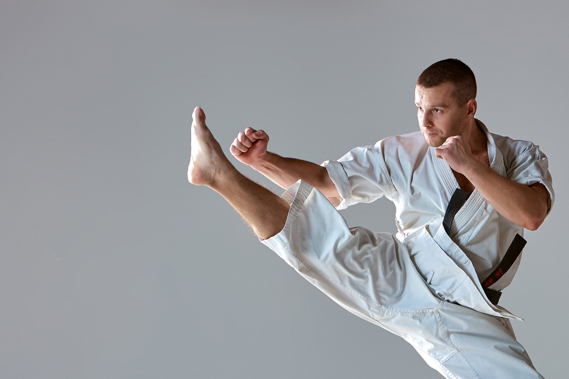 灰色背景上的跆拳道运动员白色的和服训练空手道的人
