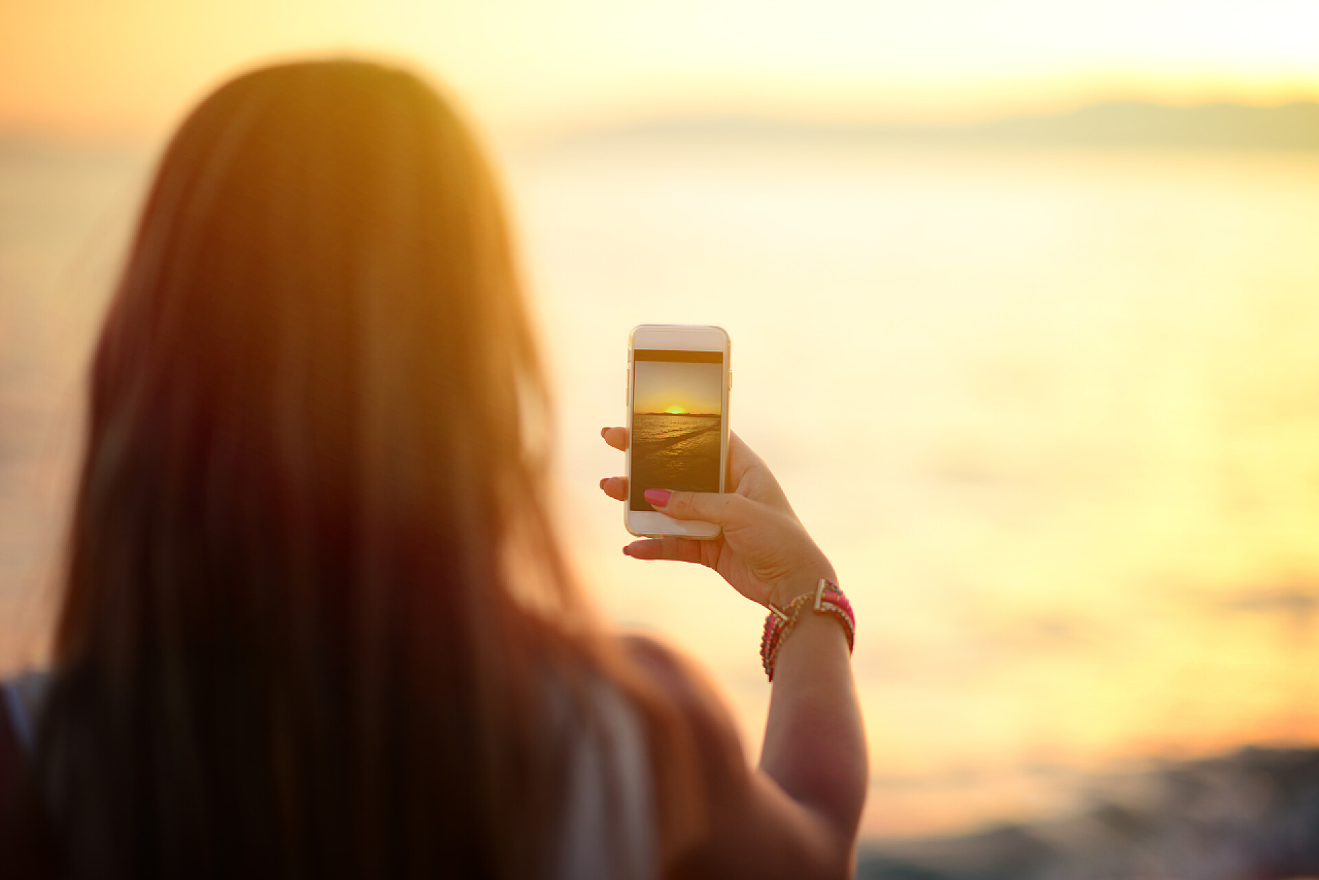 夕阳时女孩在海边拍照旅游手拿着智能手机、 拍照的美丽 b