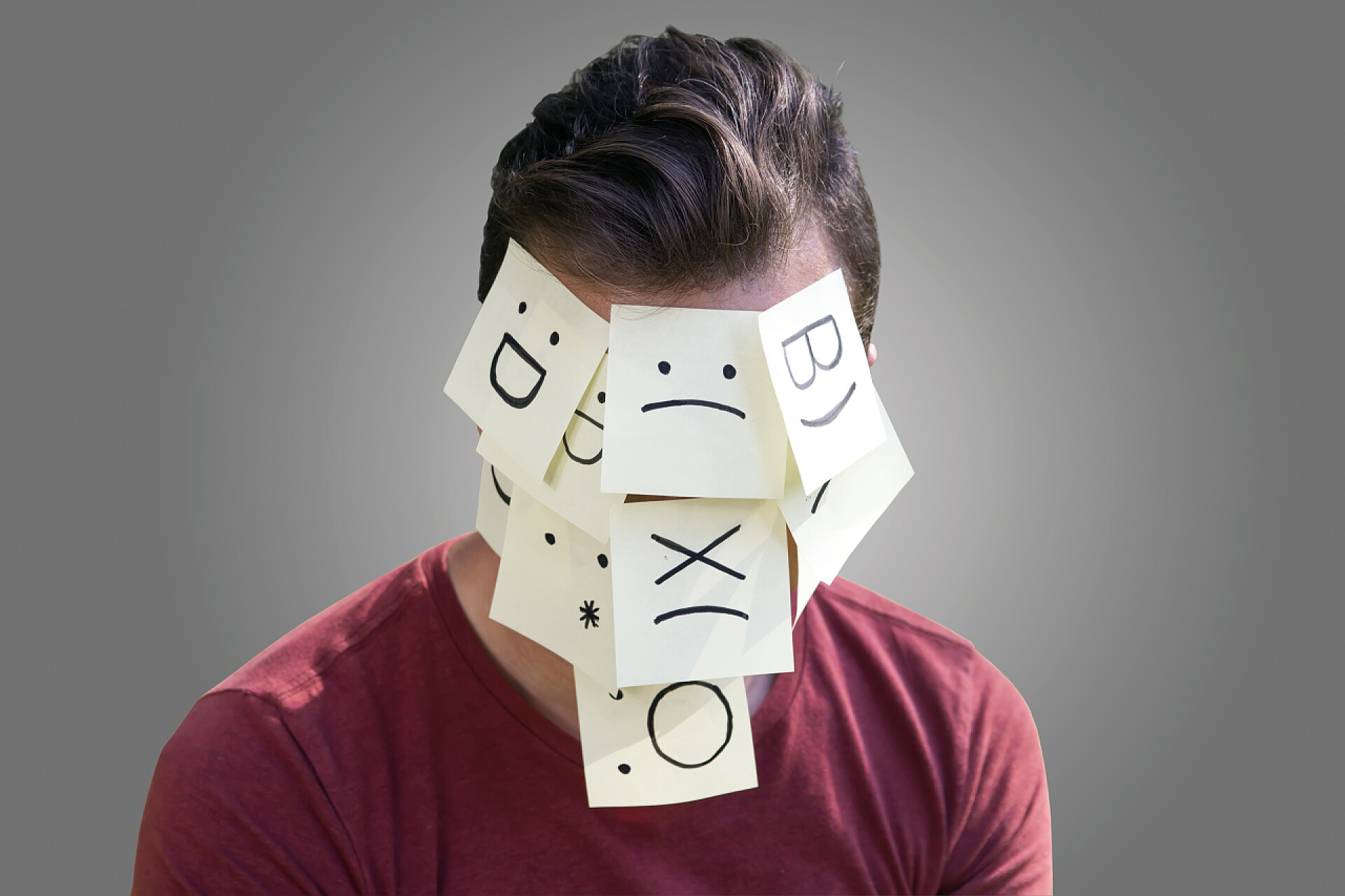 灰色背景上男人的脸上贴满了不同表情的贴纸关于思想和情感的概念。灰色的背景上孤立