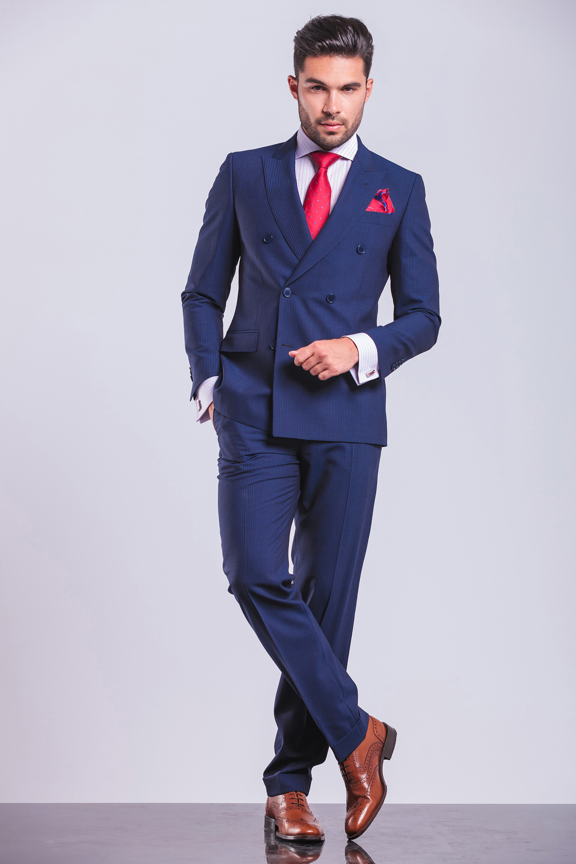 灰色背景上一个英俊的男人站立姿势全身肖像业务乔装站双腿交叉用手在口袋里