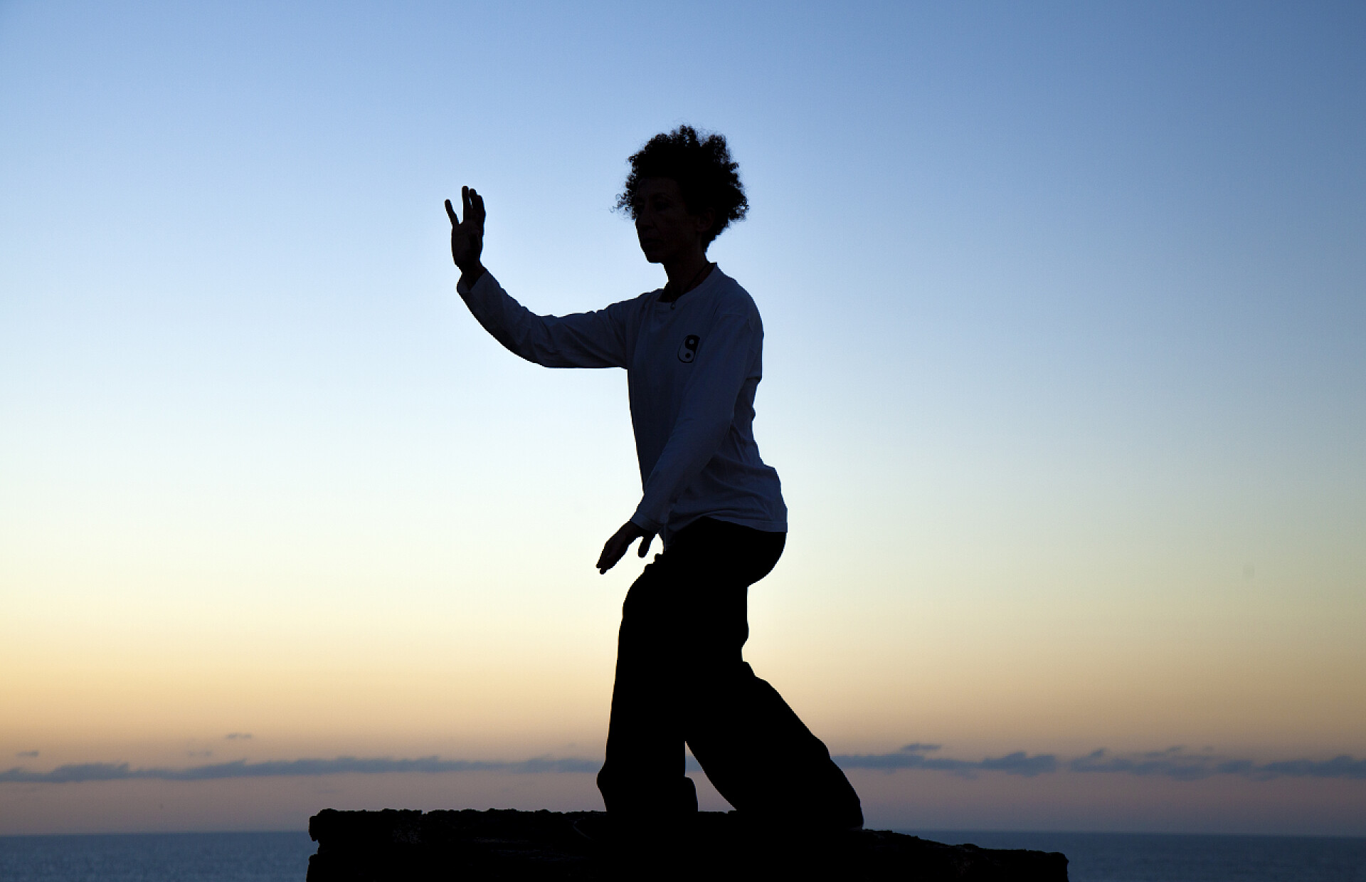 蓝色背景中一个年轻的女子打太极的剪影太极在日落时