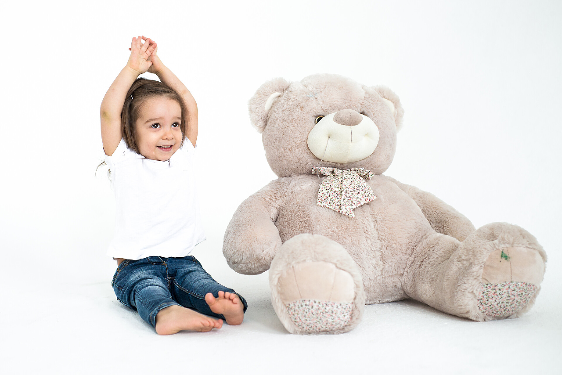 白色背景上的小女孩和玩具熊小女孩穿着白色 t 恤和牛仔裤玩，尝试用她妈妈的高跟鞋