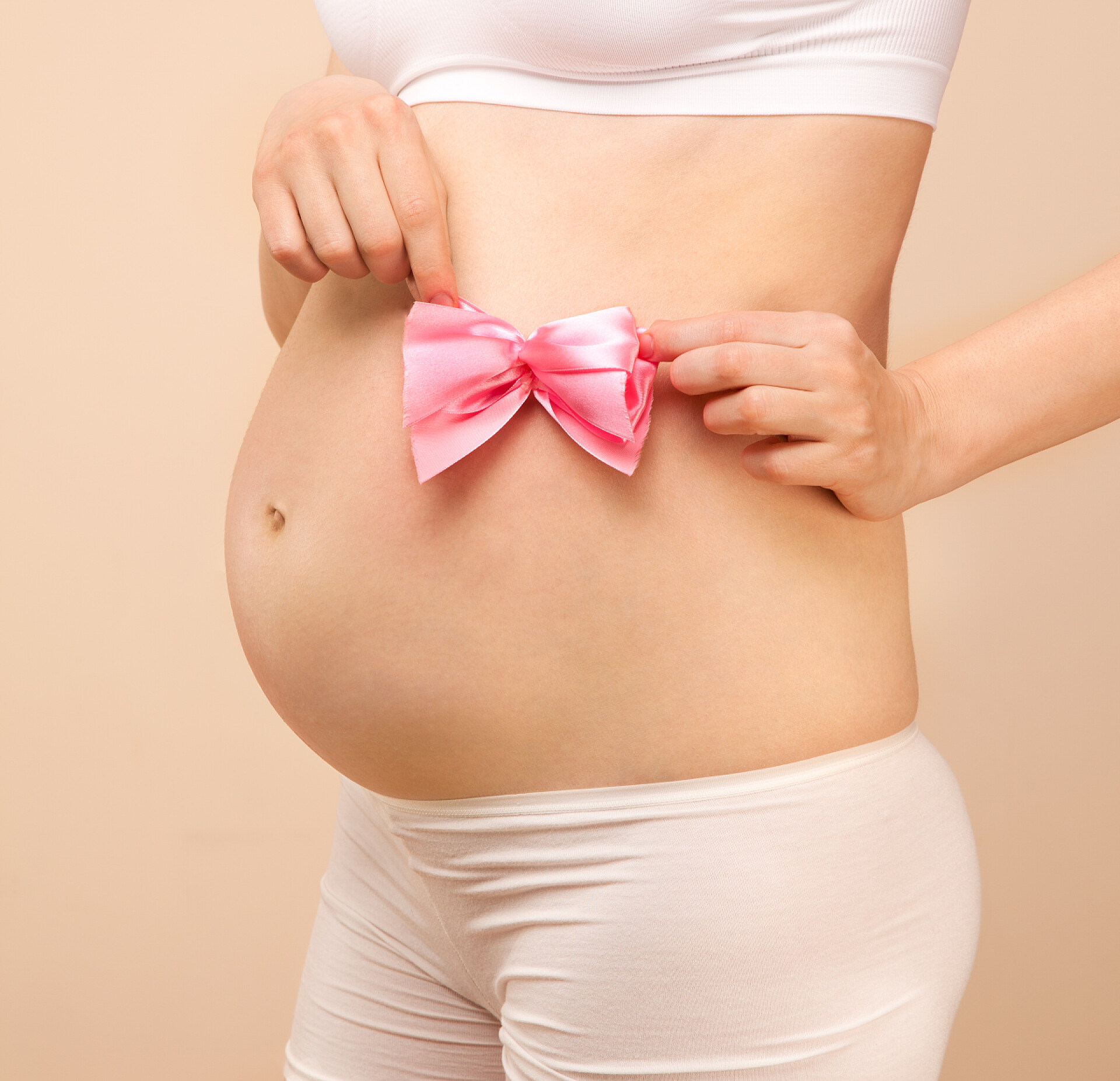 孕肚旁边拿粉红色蝴蝶结的双手孕妇的肚子有粉红色蝴蝶结