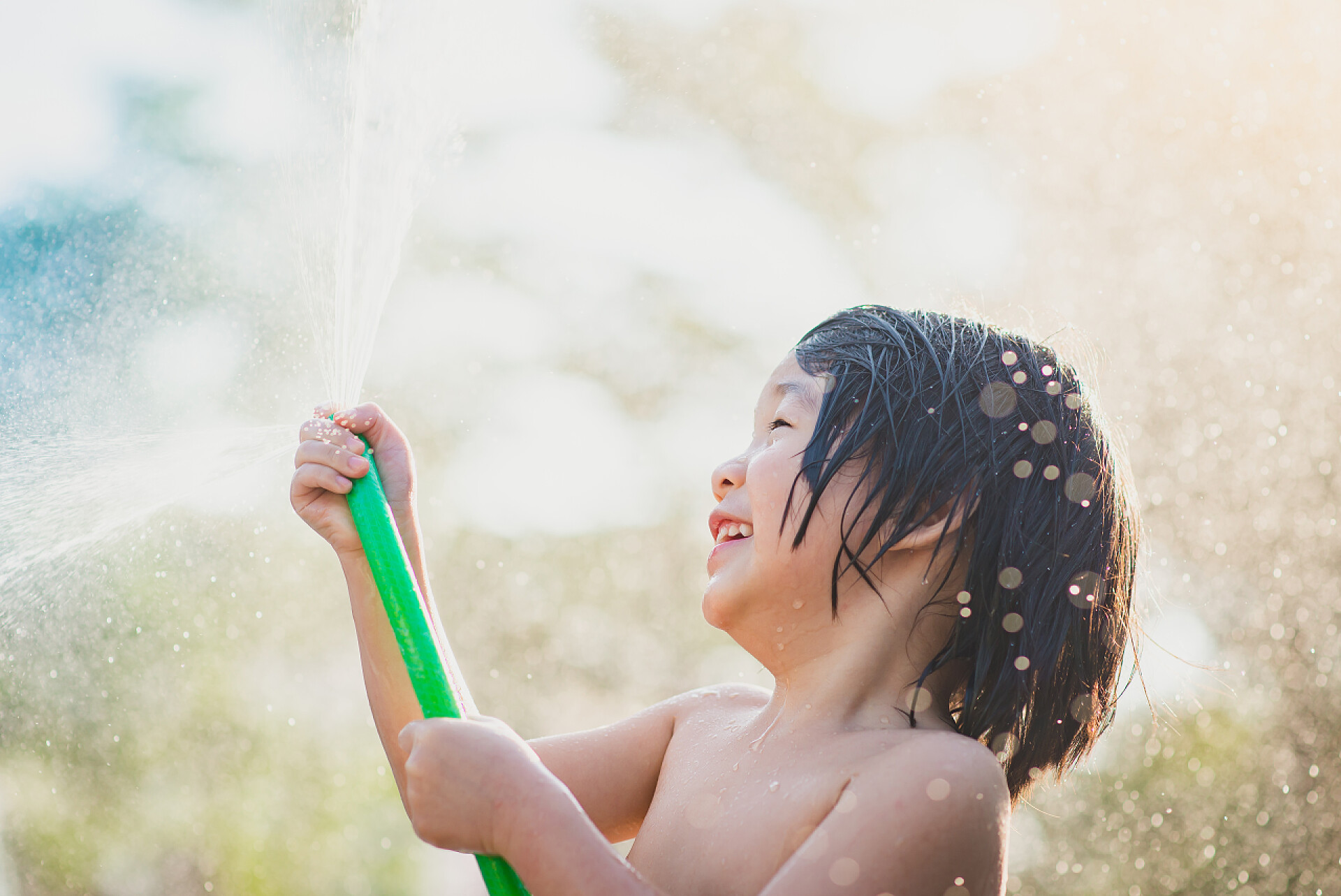 男孩在户外用软管玩水很开心可爱的亚洲男孩在户外用软管玩水很开心