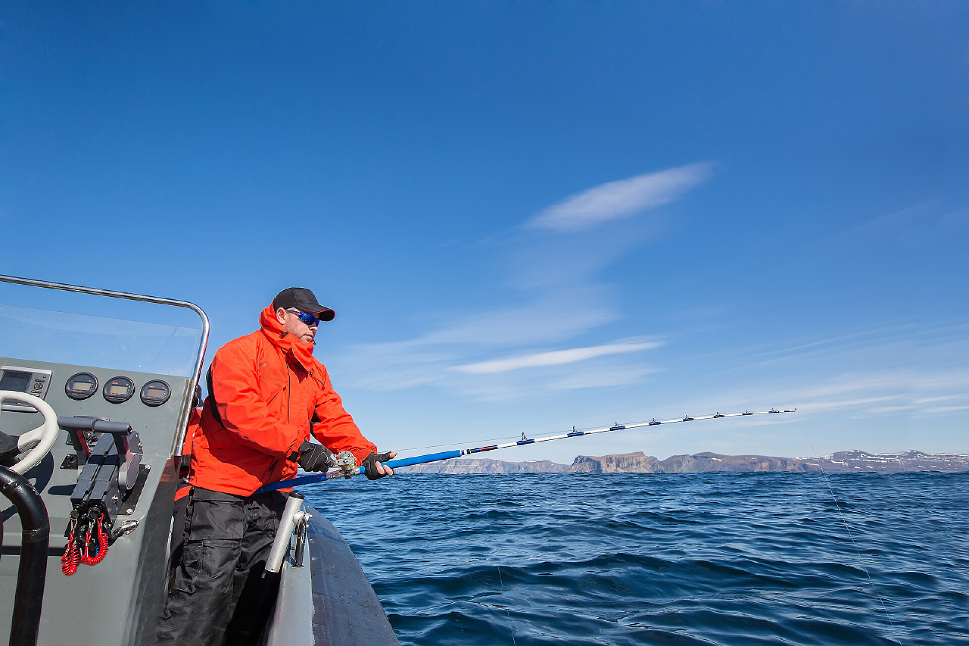 在蓝色大海边钓鱼的男人从船钓竿钓鱼的人。红夹克.