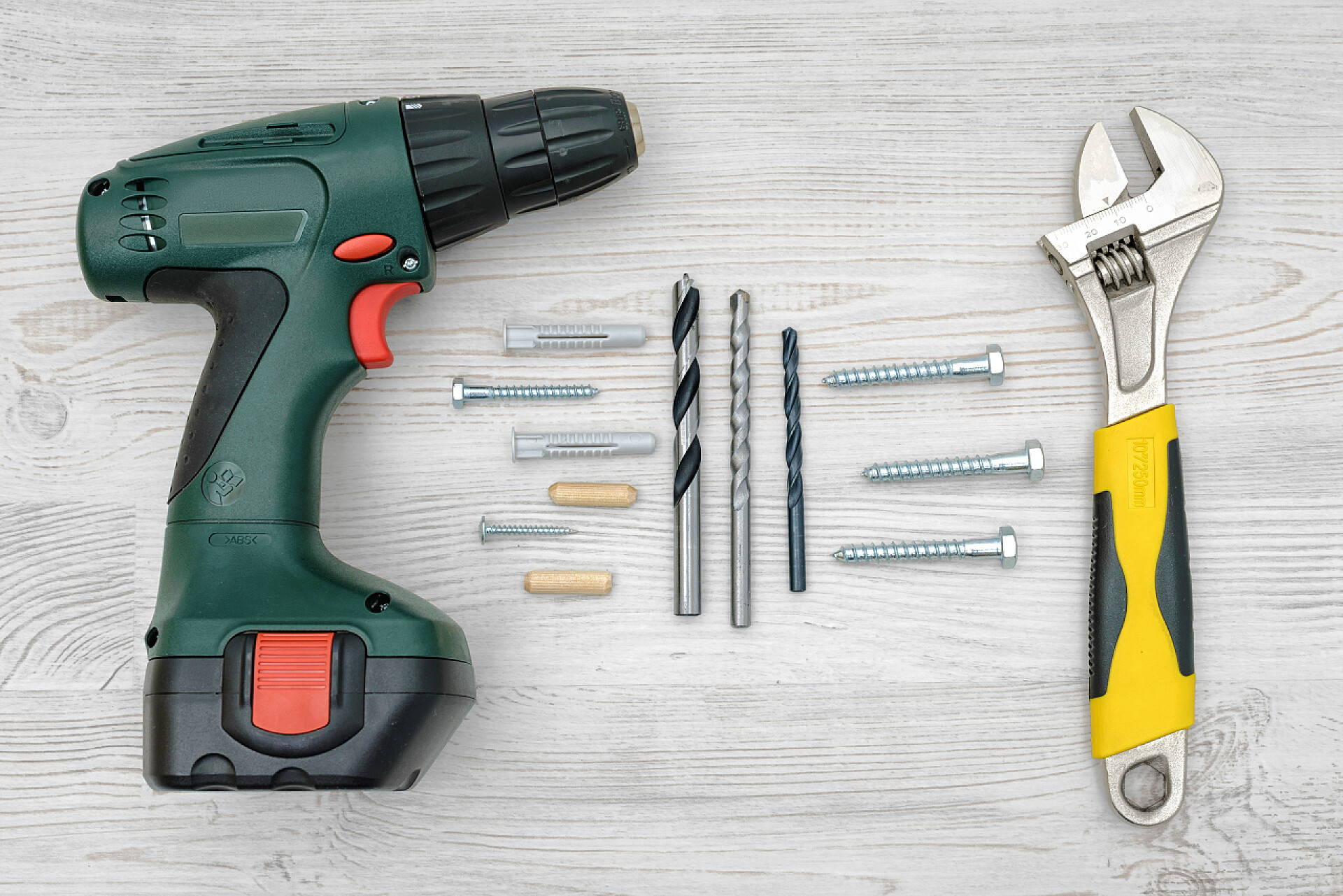 桌面上的手枪钻和扳手充电式电钻、 扳手、 几个钻头、 螺栓和销钉上光木背景.