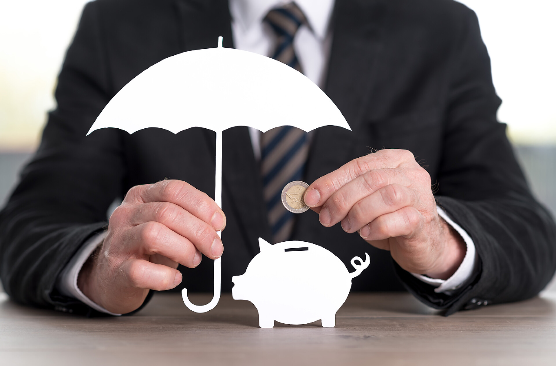 男人举着伞把金币放入存钱罐保存保护的概念