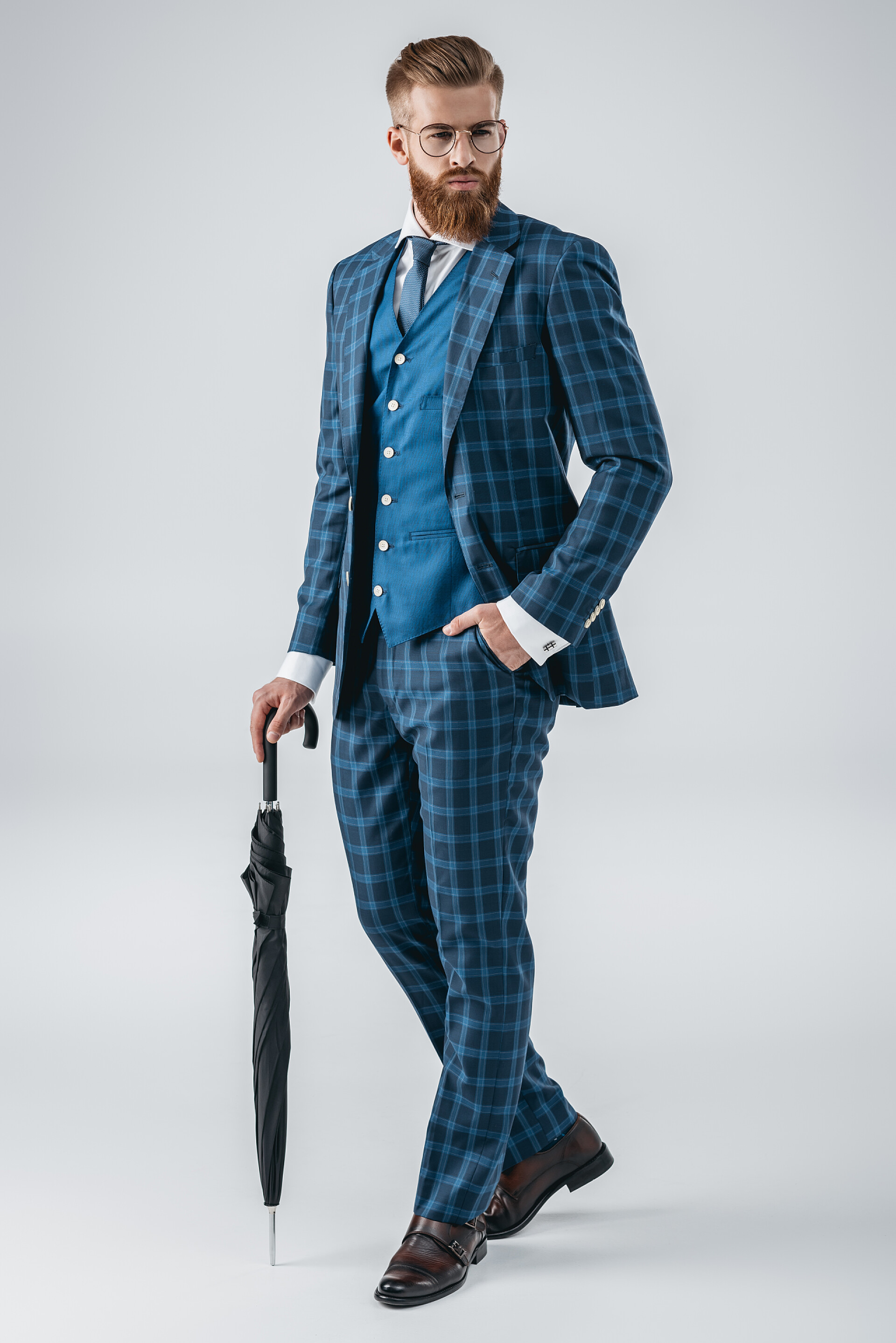 灰色背景上拿着雨伞插着口袋的时尚商人时髦的年轻人用的伞