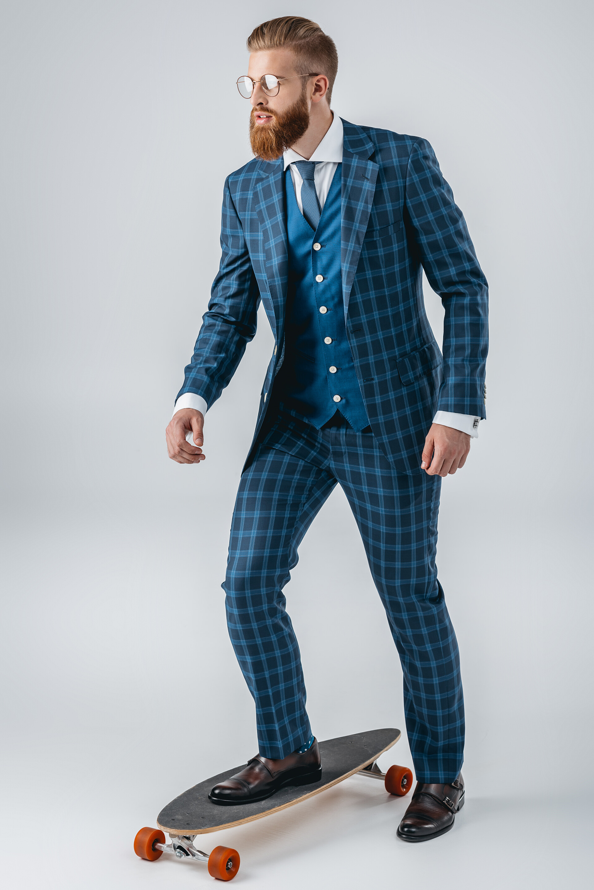 灰色背景上玩滑板的商人穿着西装在滑板上的时尚男人