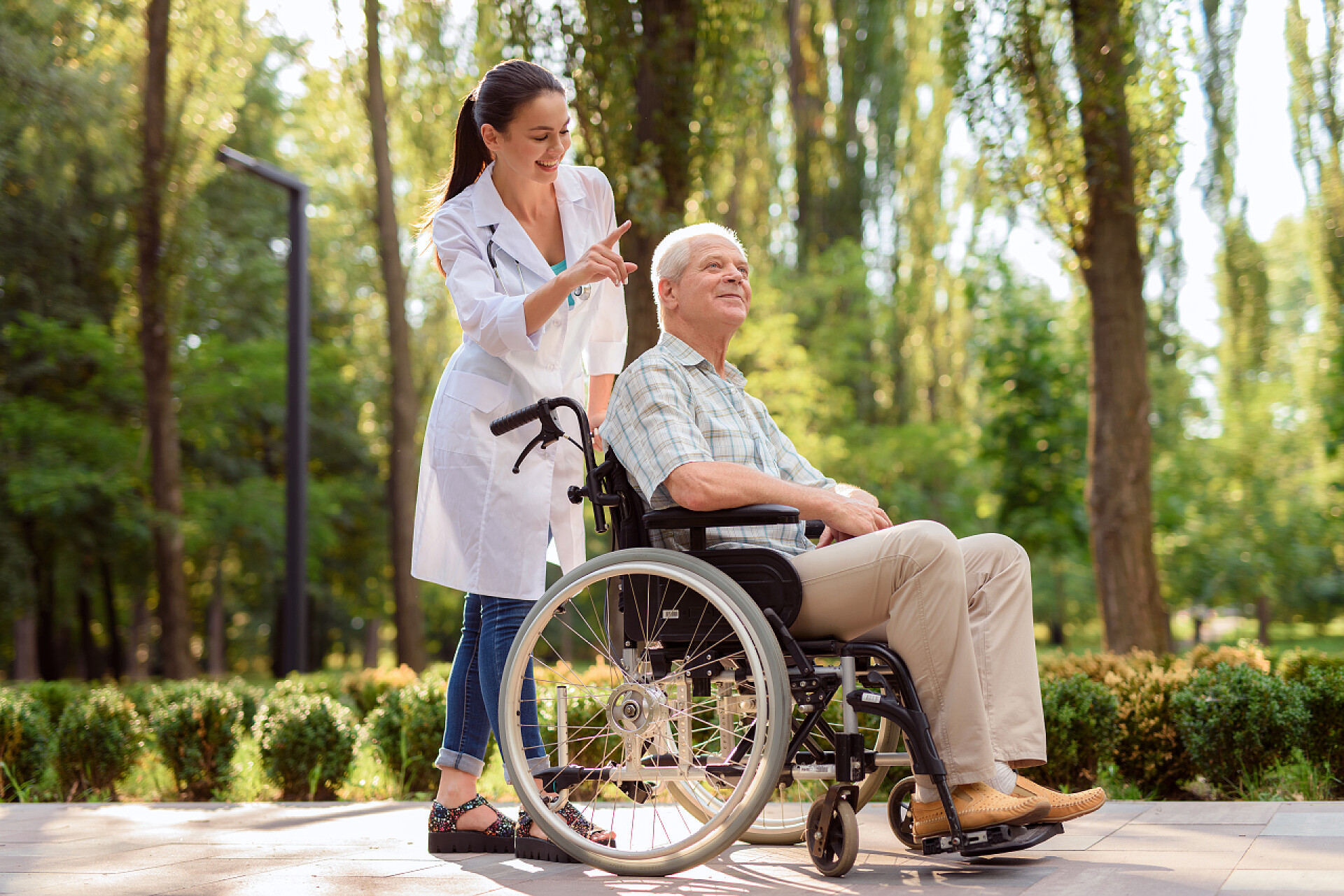 一个医生推着坐在轮椅上的老爷爷在阳光明媚的公园里坐在轮椅上微笑的老人