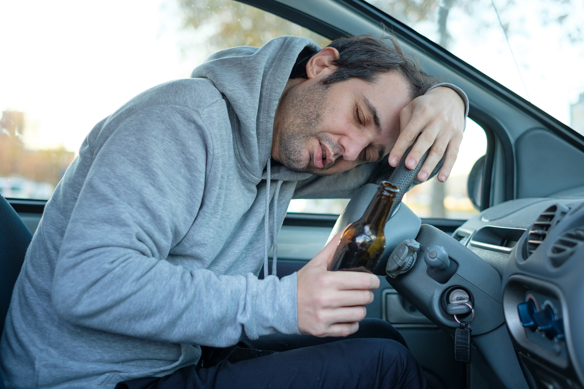 一个男人喝醉了倒在主驾驶的方向盘上年轻男子驾驶他的车, 而饮酒和下降的手语