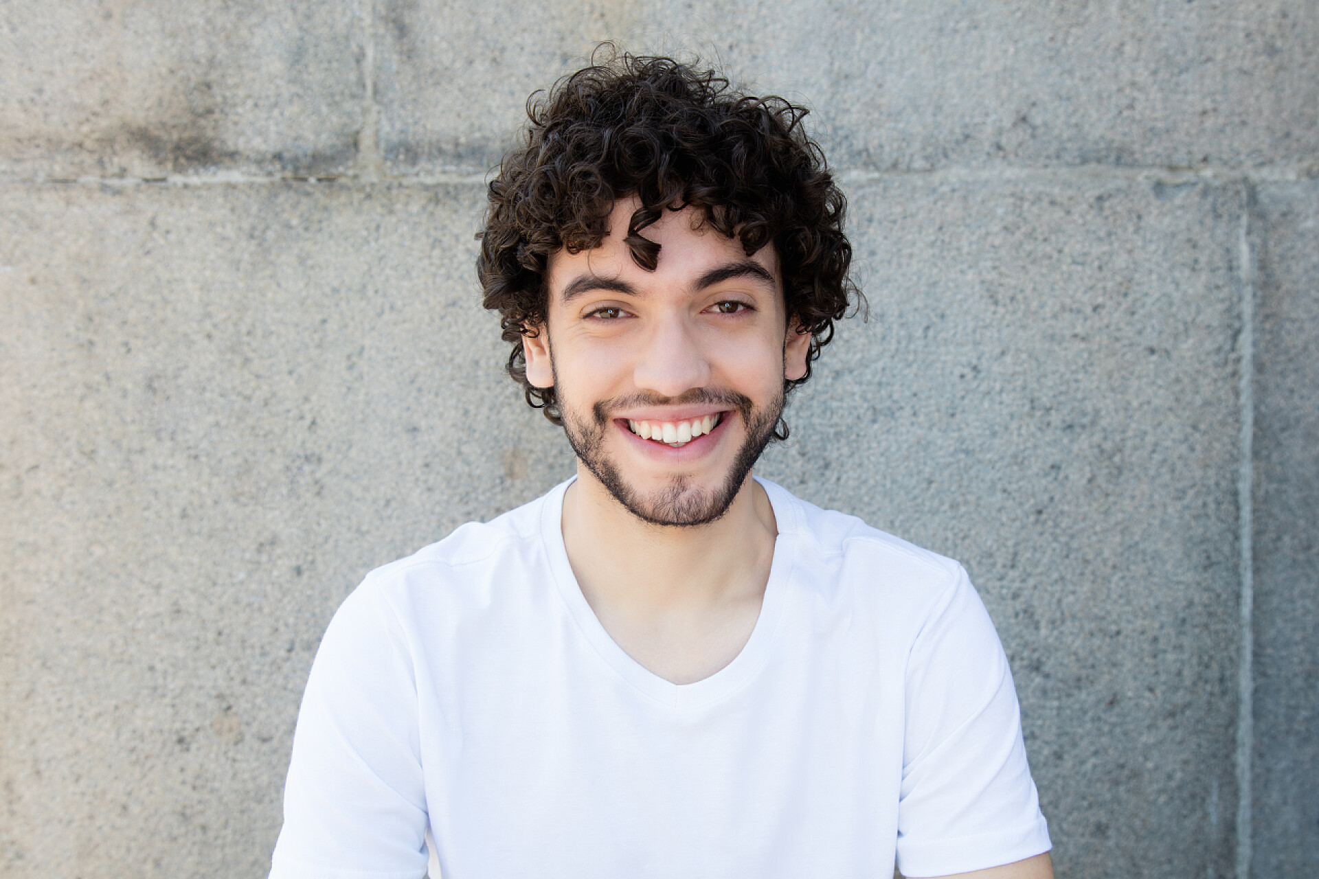 墙壁间一个穿着白色短袖的男人看着镜头微笑一个英俊的白种人年轻的成年男子胡子的肖像