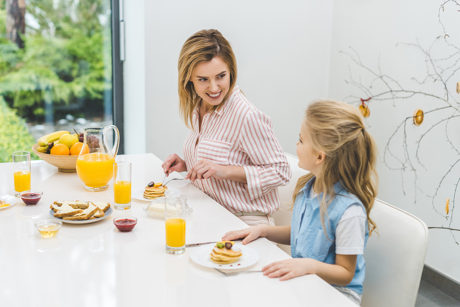 白色的餐桌上吃饭的母女微笑的母亲和女儿在家一起吃早餐