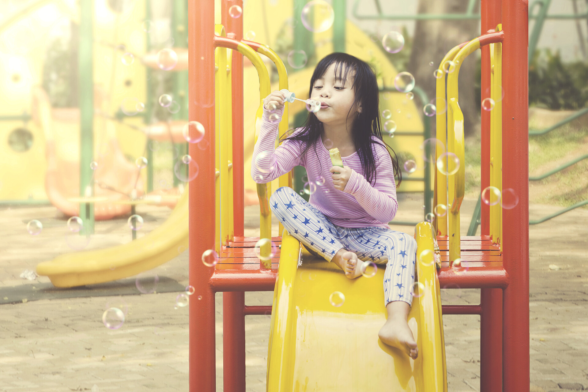 在滑地上吹着泡泡的小女孩小女孩在操场上玩肥皂泡。夏季和春季概念