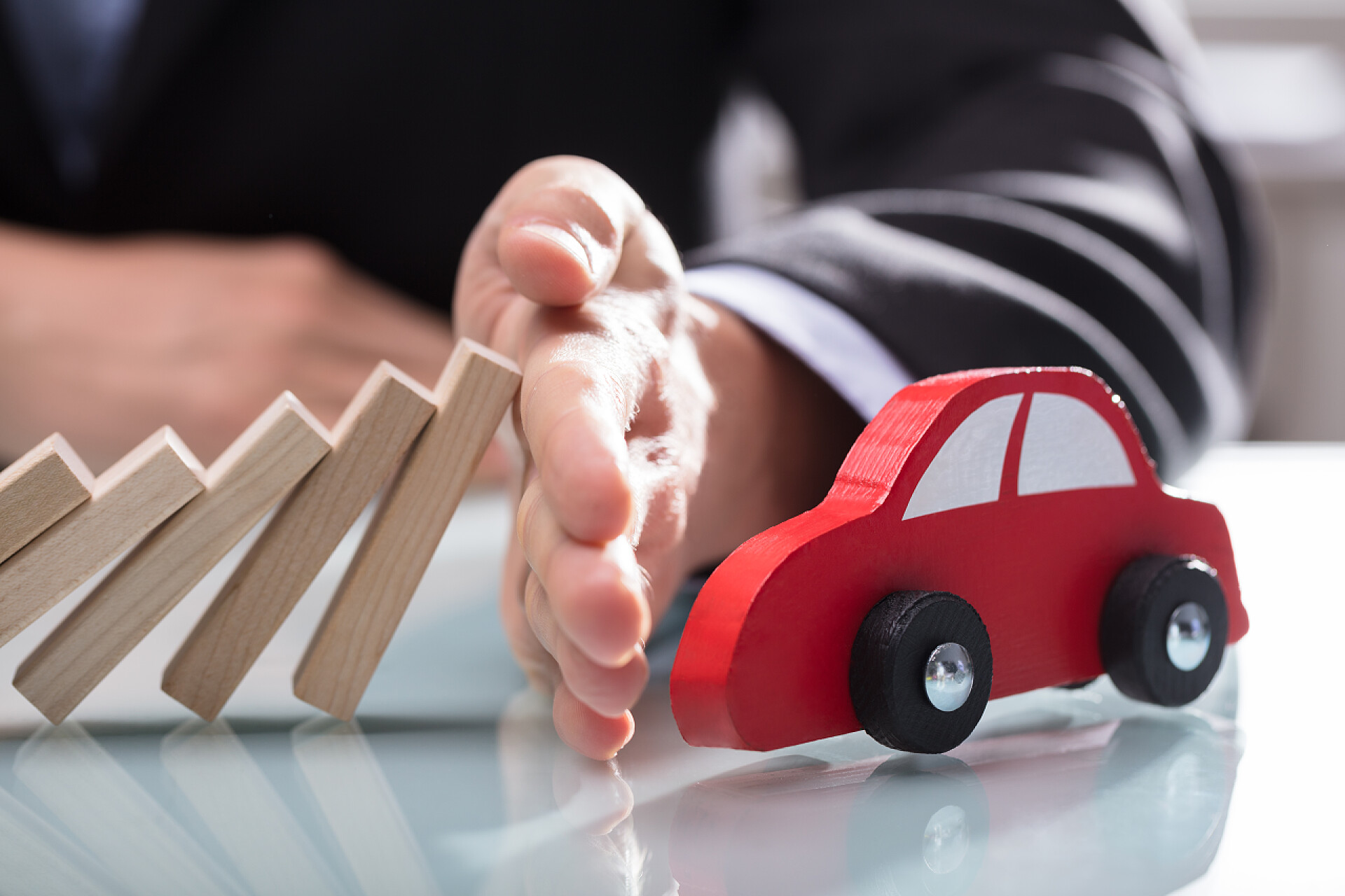 白色小桌上的多米诺骨牌和小车关闭了一个商人的手停止木块下跌的红色汽车在办公桌上