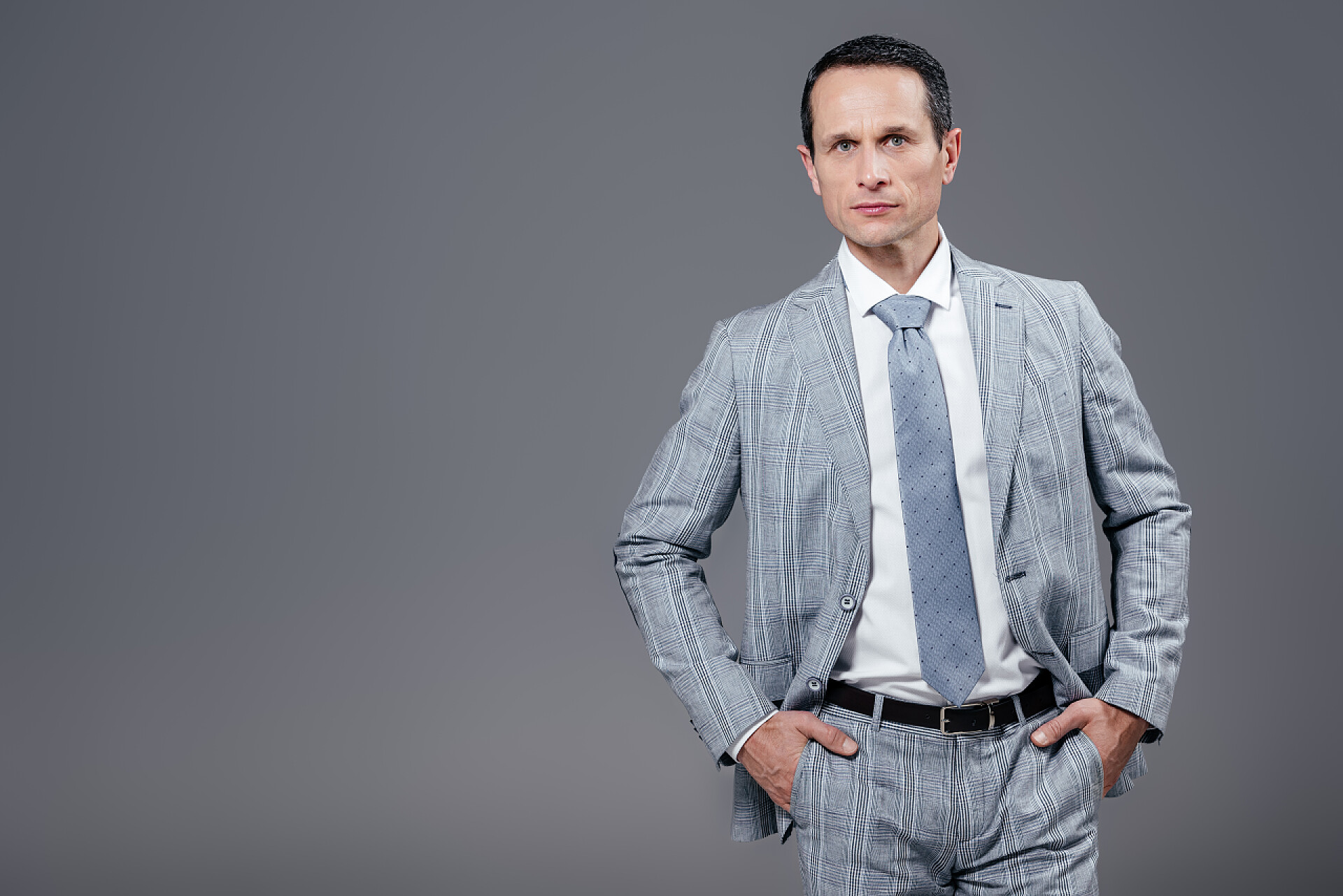 灰色背景墙前站着一个英俊的男人英俊的成年商人在时尚西装看着相机孤立的灰色