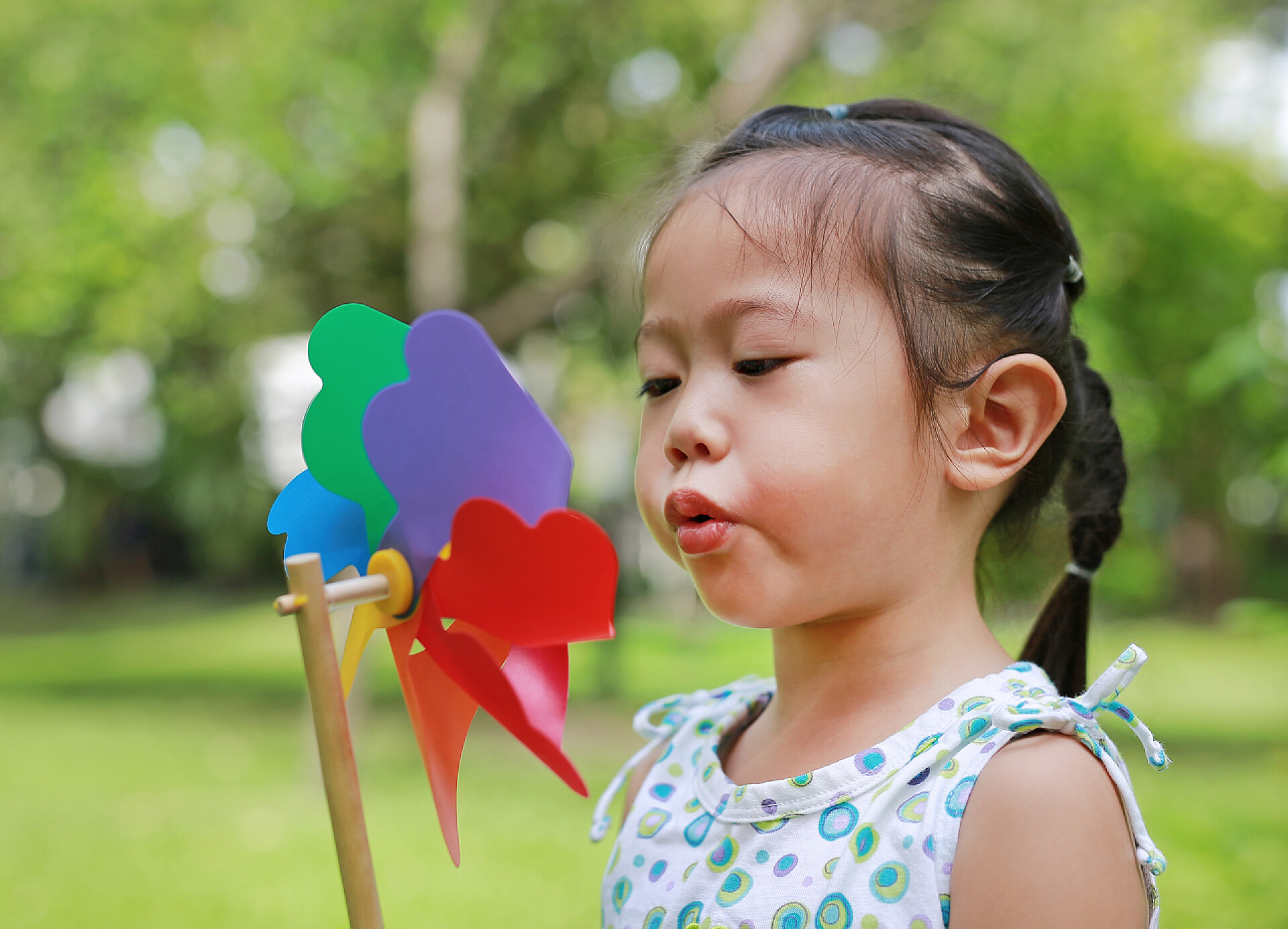 可爱的小女孩在吹着小风车可爱的小女孩吹风力涡轮机在花园里