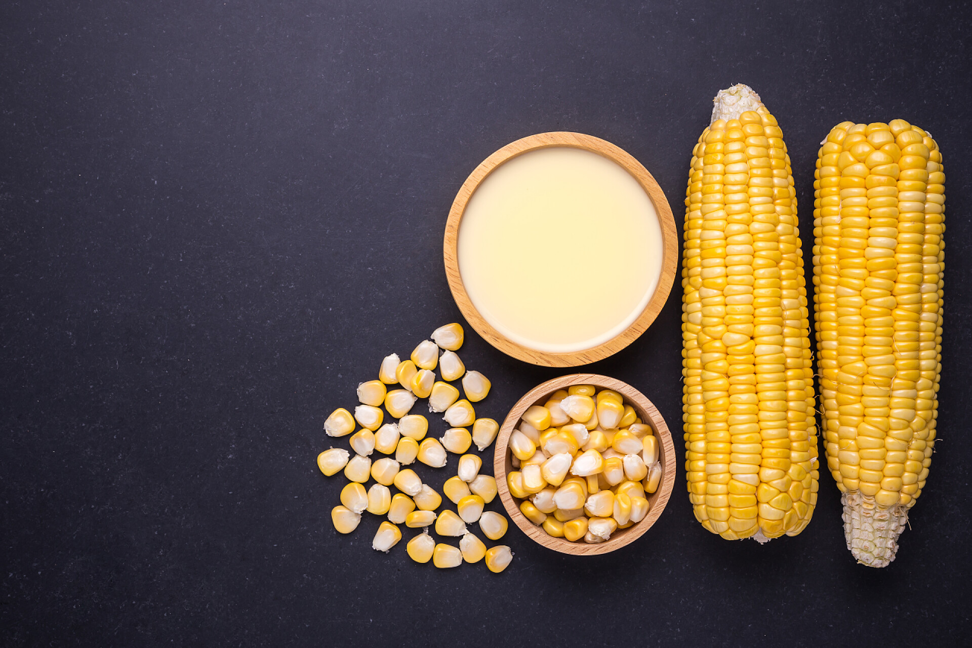 黑色桌子上的玉米和玉米粒玉米糊鲜黄色甜玉米棒和玉米汁
