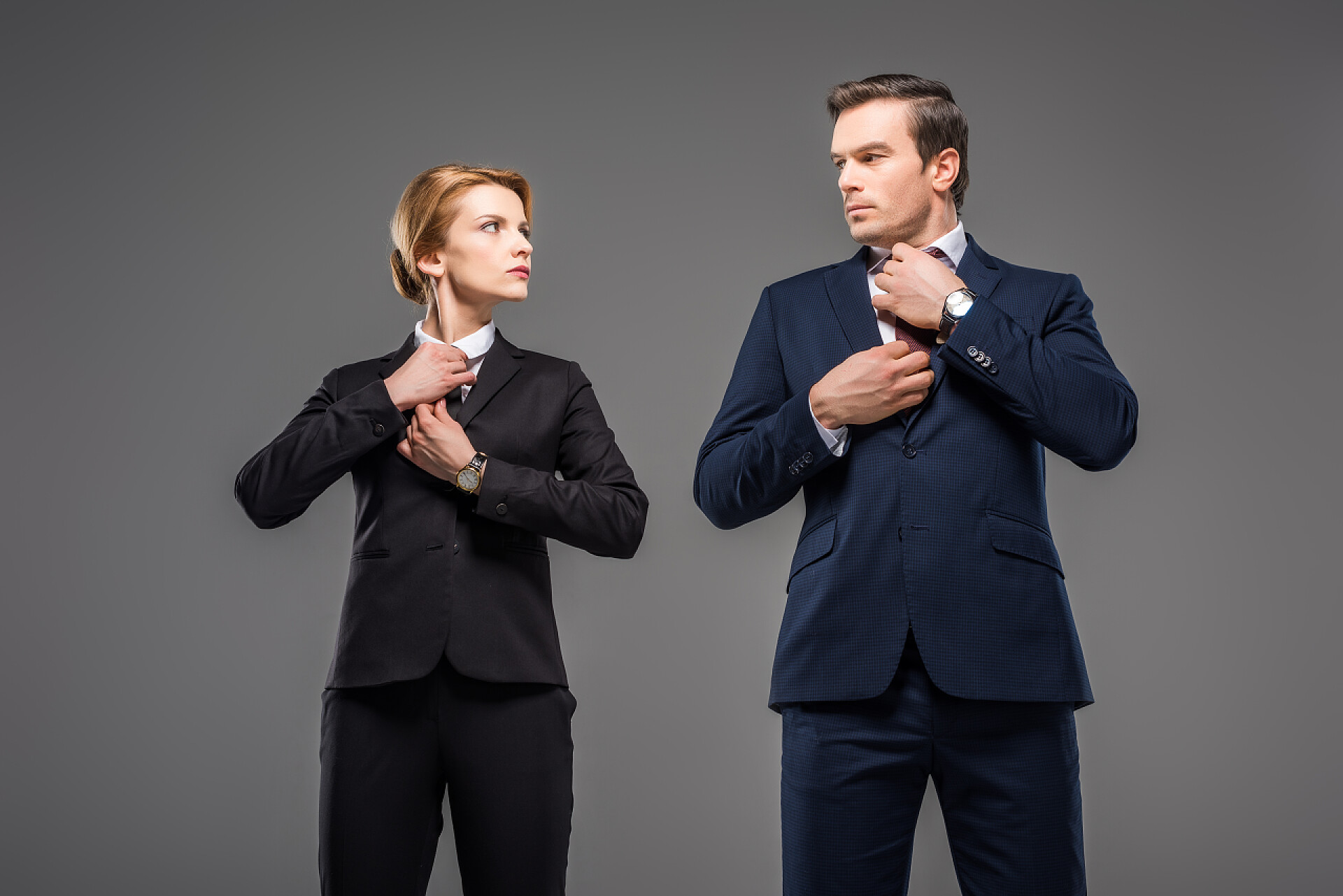 灰色背景墙的两个人在暗暗较劲认真的商人和商人固定联系, 看着对方, 孤立的灰色, 女权主义的概念