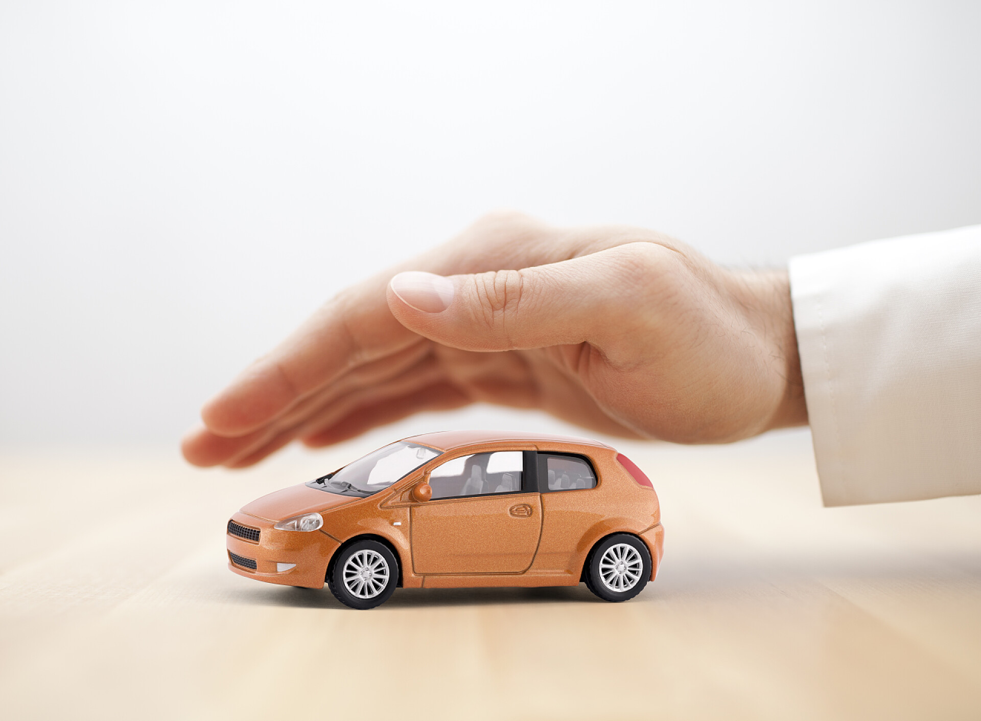 木制的桌子上一只手在护着一辆汽车模型汽车保险概念。手盖小玩具车