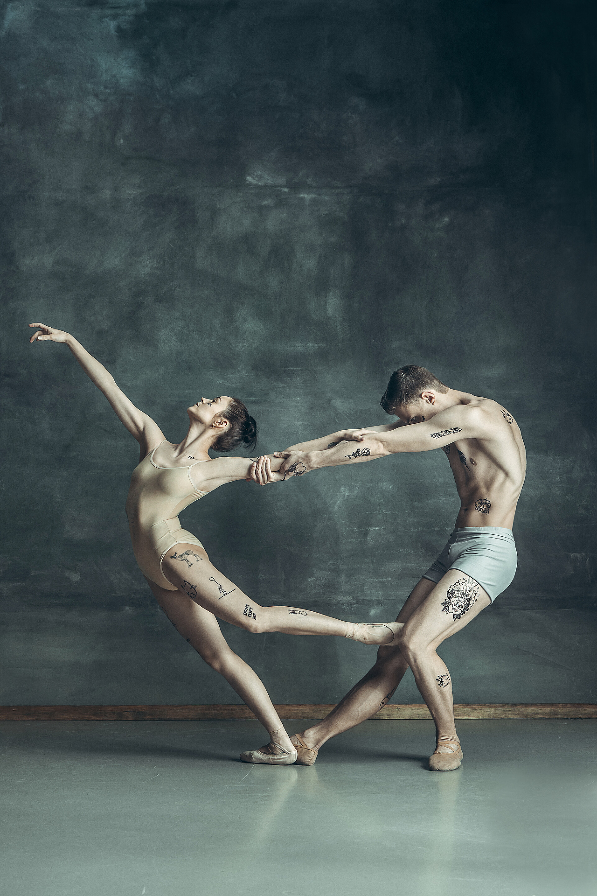 在黑灰墙前舞动的男女年轻的现代芭蕾舞演员在灰色演播室背景上摆姿势