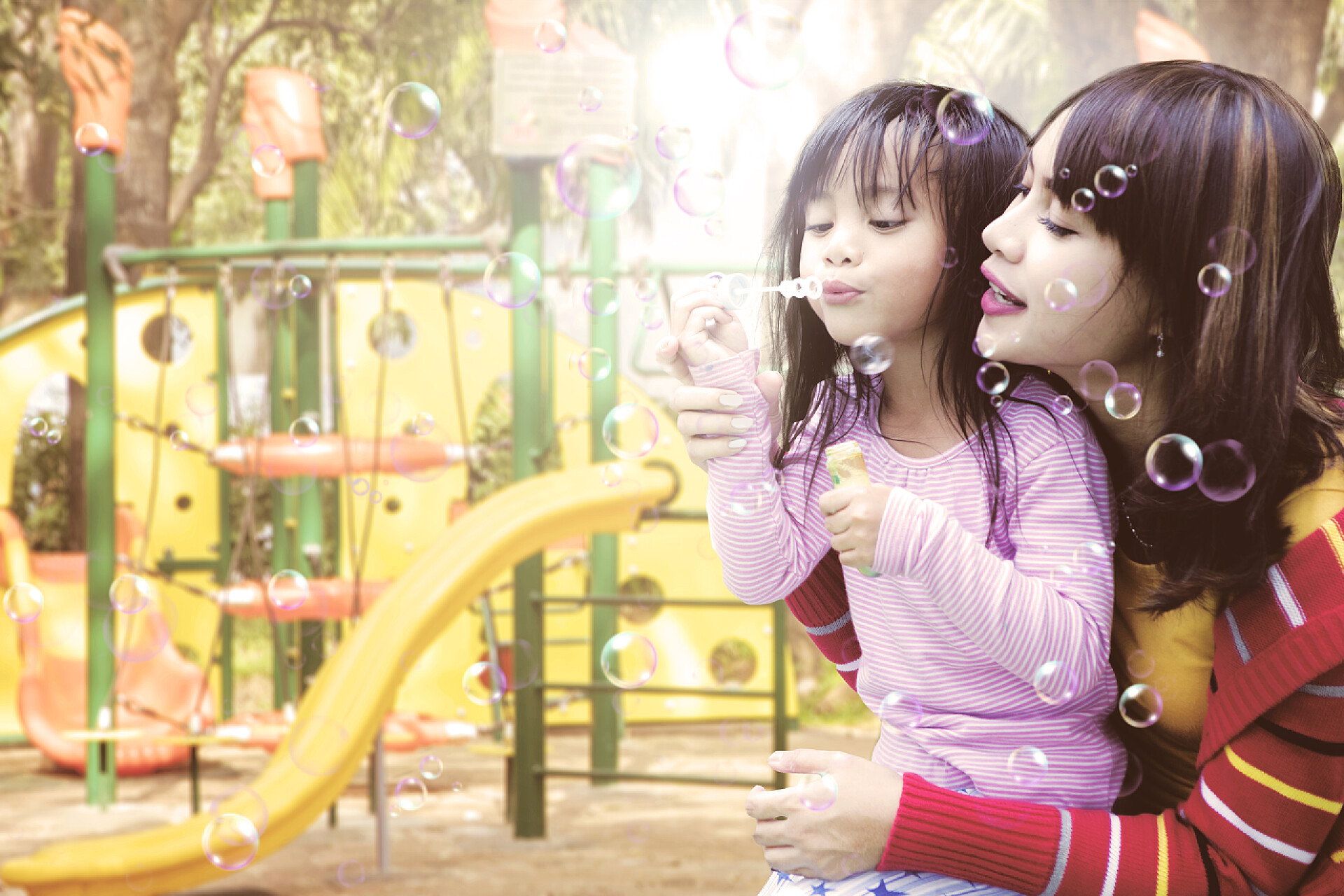 妈妈陪着女儿在吹泡泡母亲和女儿在操场上吹肥皂泡的乐趣