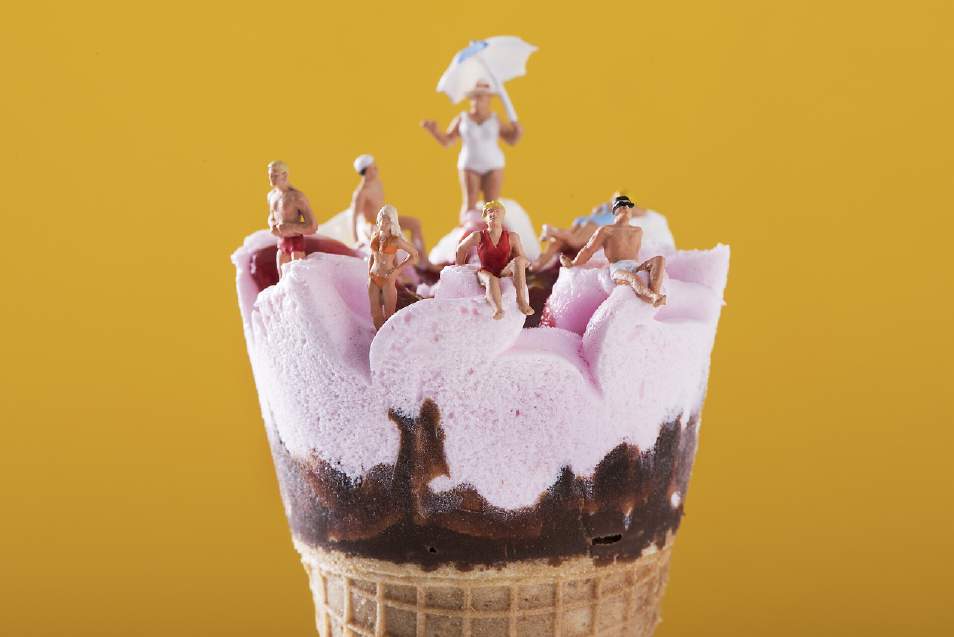 黄色背景下的冰淇淋特写的一些迷你的人穿着泳装放松在预先填充的冰淇淋锥, 对橙色背景