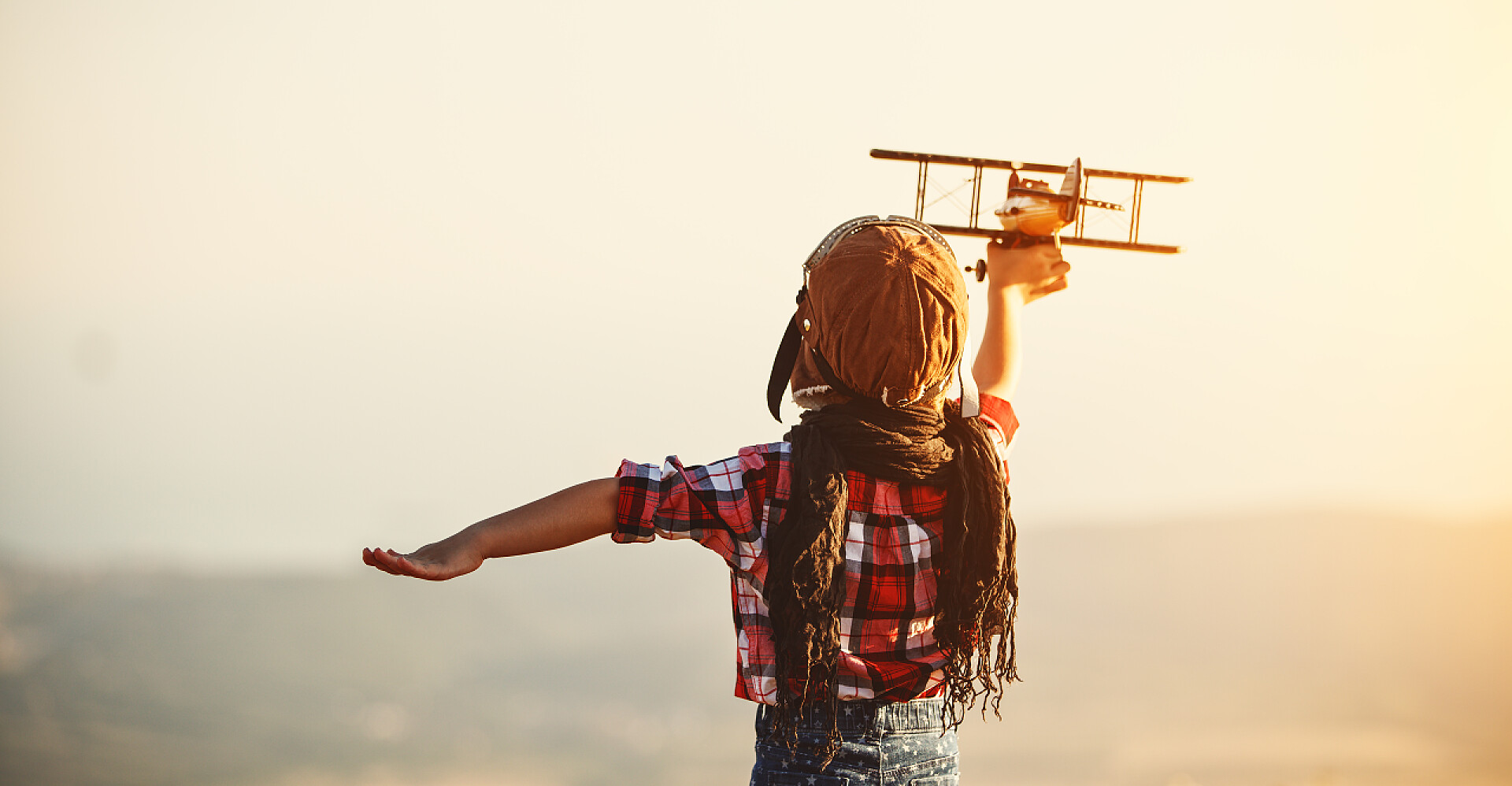一个小孩子拿着木制飞机在玩飞行员与飞机梦想在夏天旅行在自然日落