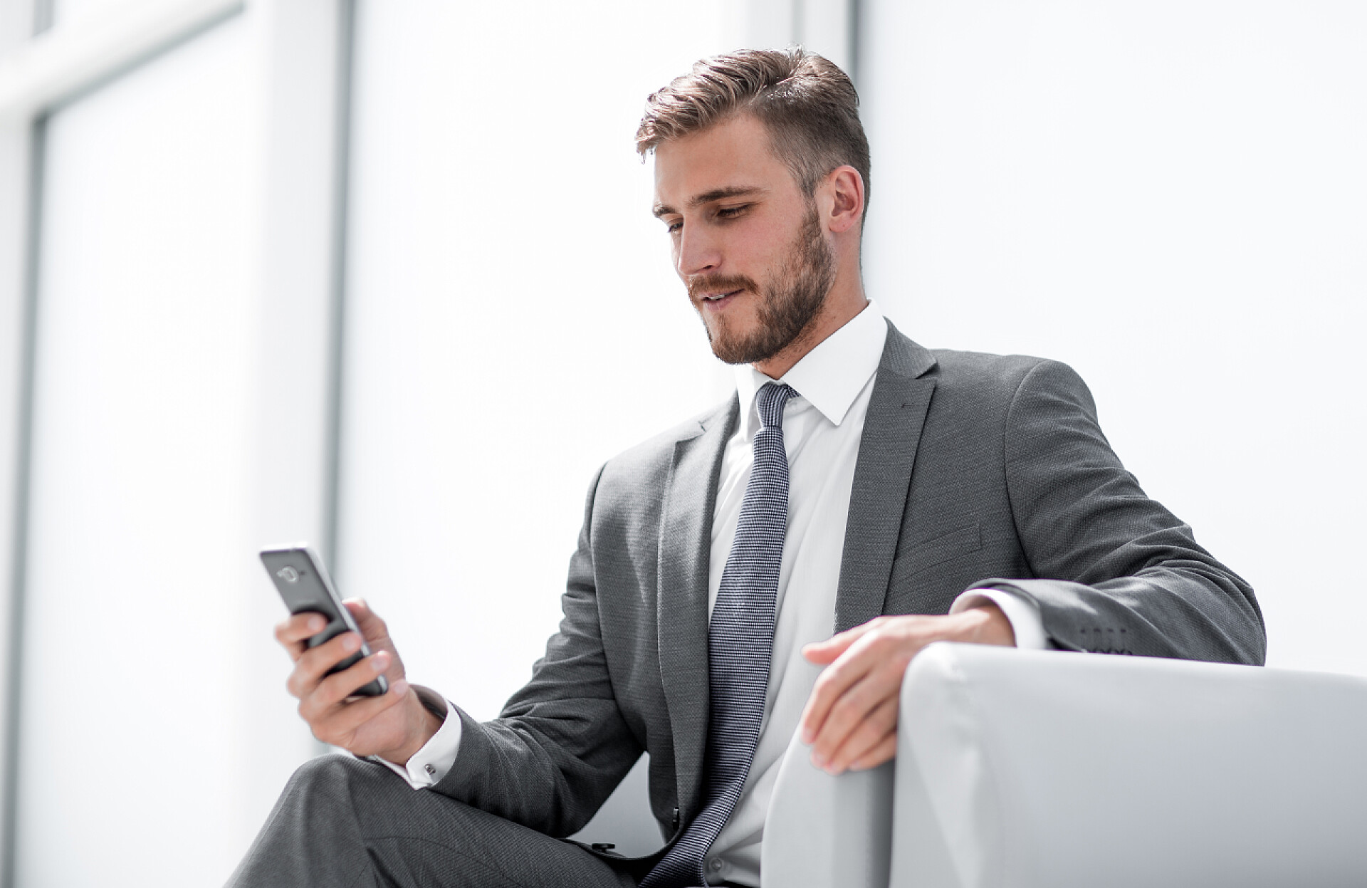 一个男人穿着西服坐在沙发上玩手机英俊的商人在小工具工作.